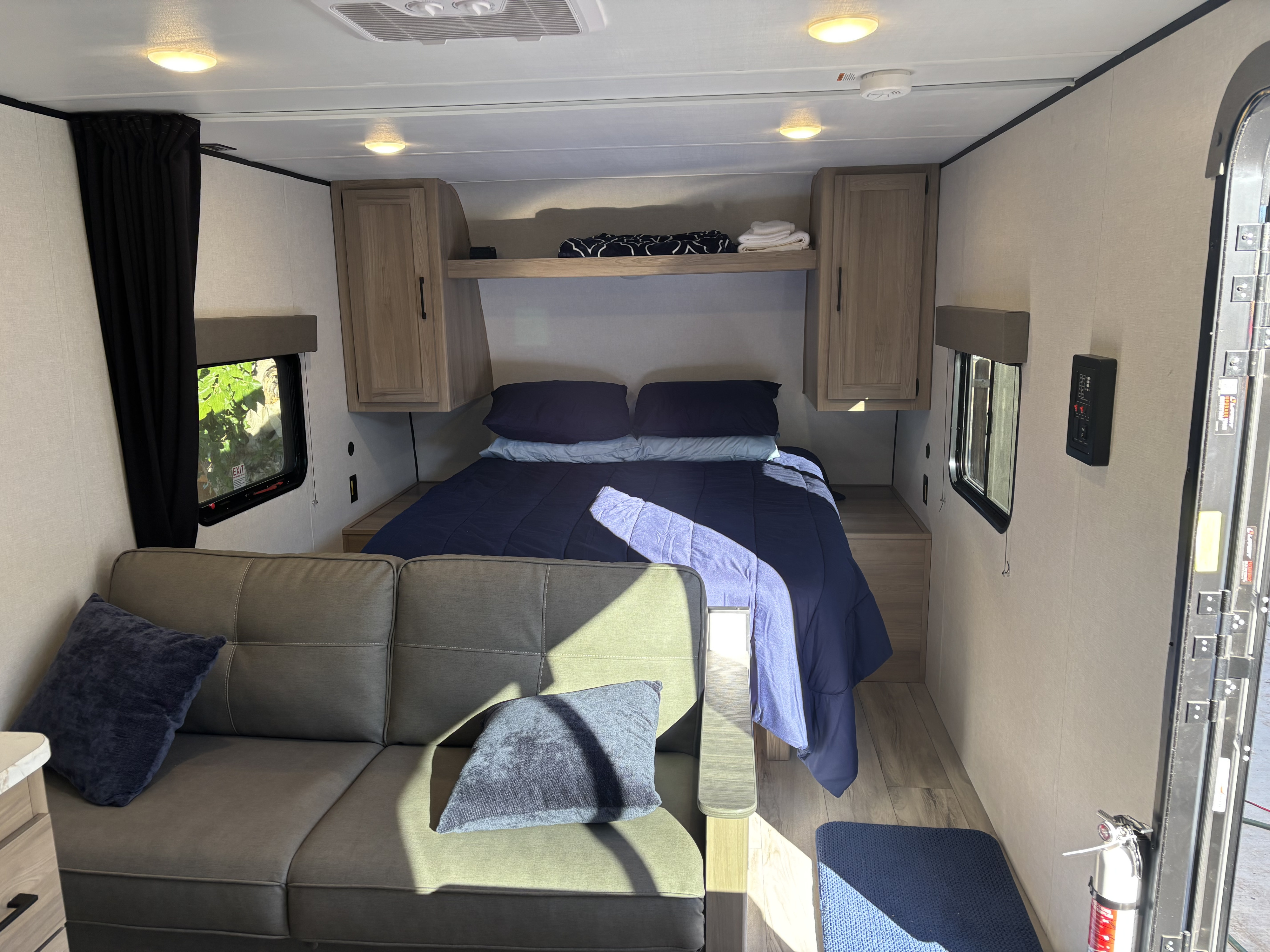 View of a modern rv rental interior, showing a cozy bed, sofa, windows, and compact living space with natural light.. Coleman Coleman 23 B 2025