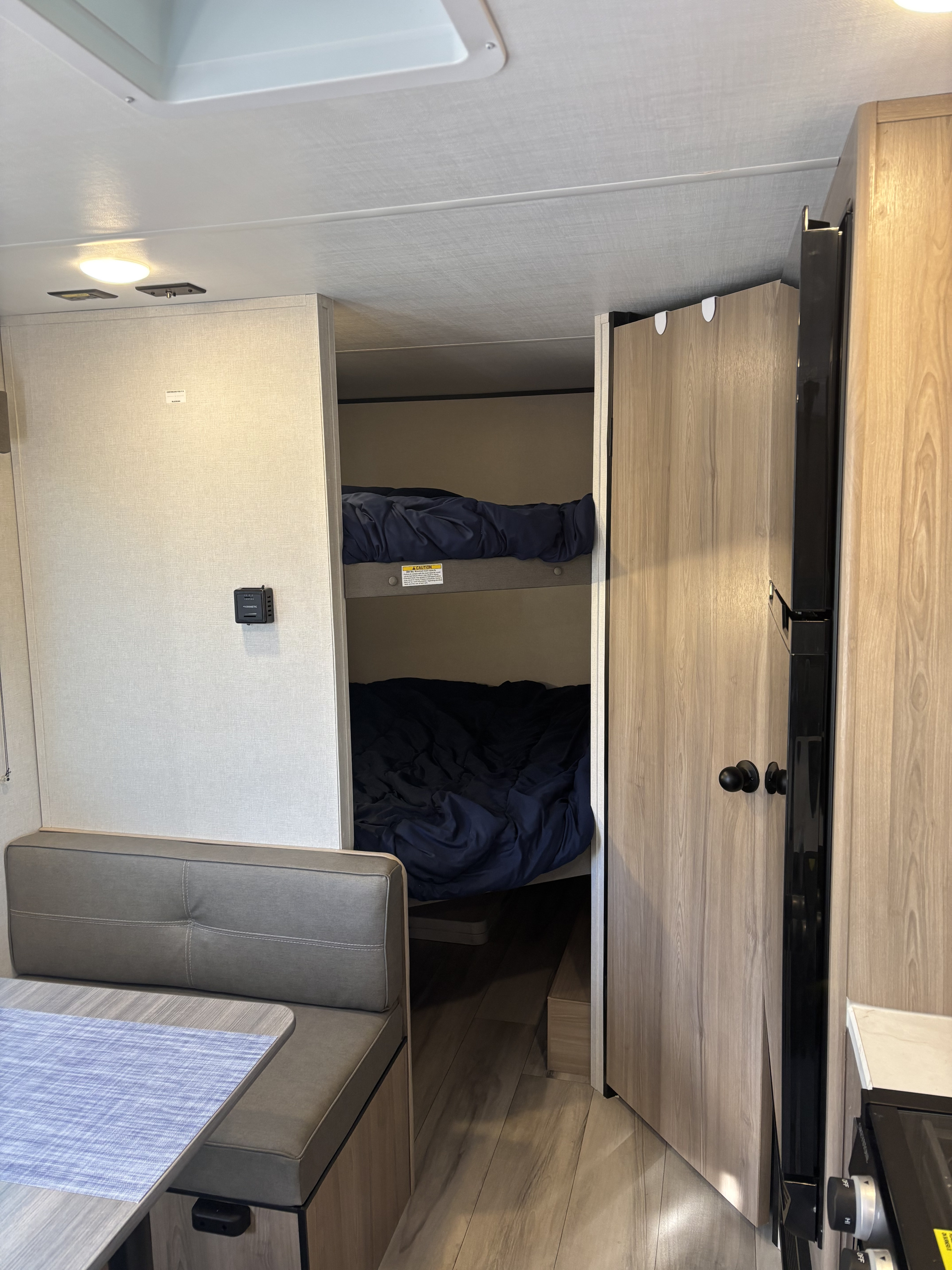 RV rental interior with a gray dinette, two dark blue bunk beds, and glimpse of a kitchen.. Coleman Coleman 23 B 2025