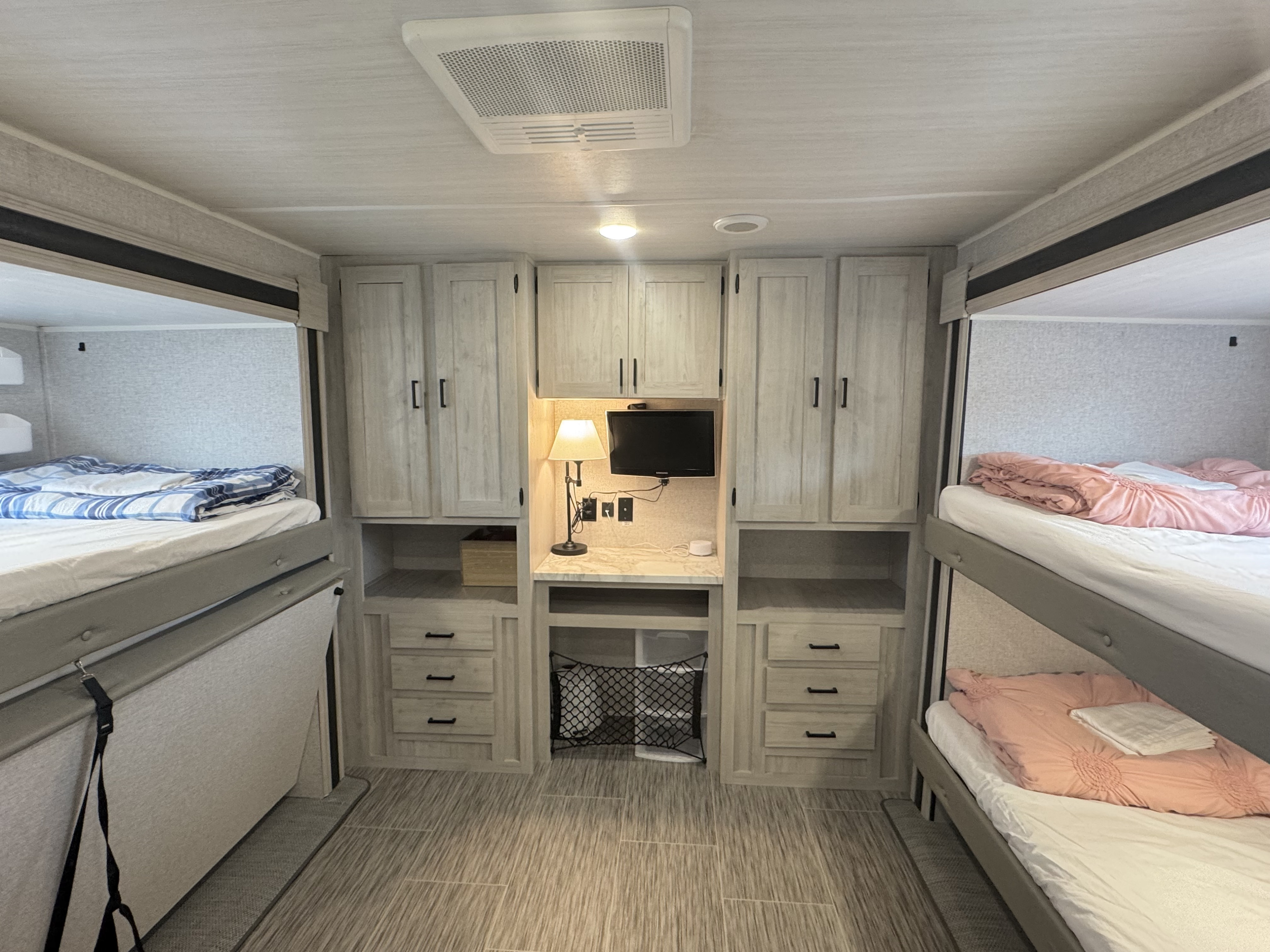 Spacious RV rental interior featuring two sets of bunk beds, central storage, and a desk area for comfortable travel accommodation.. East to West Silver Lake 2022