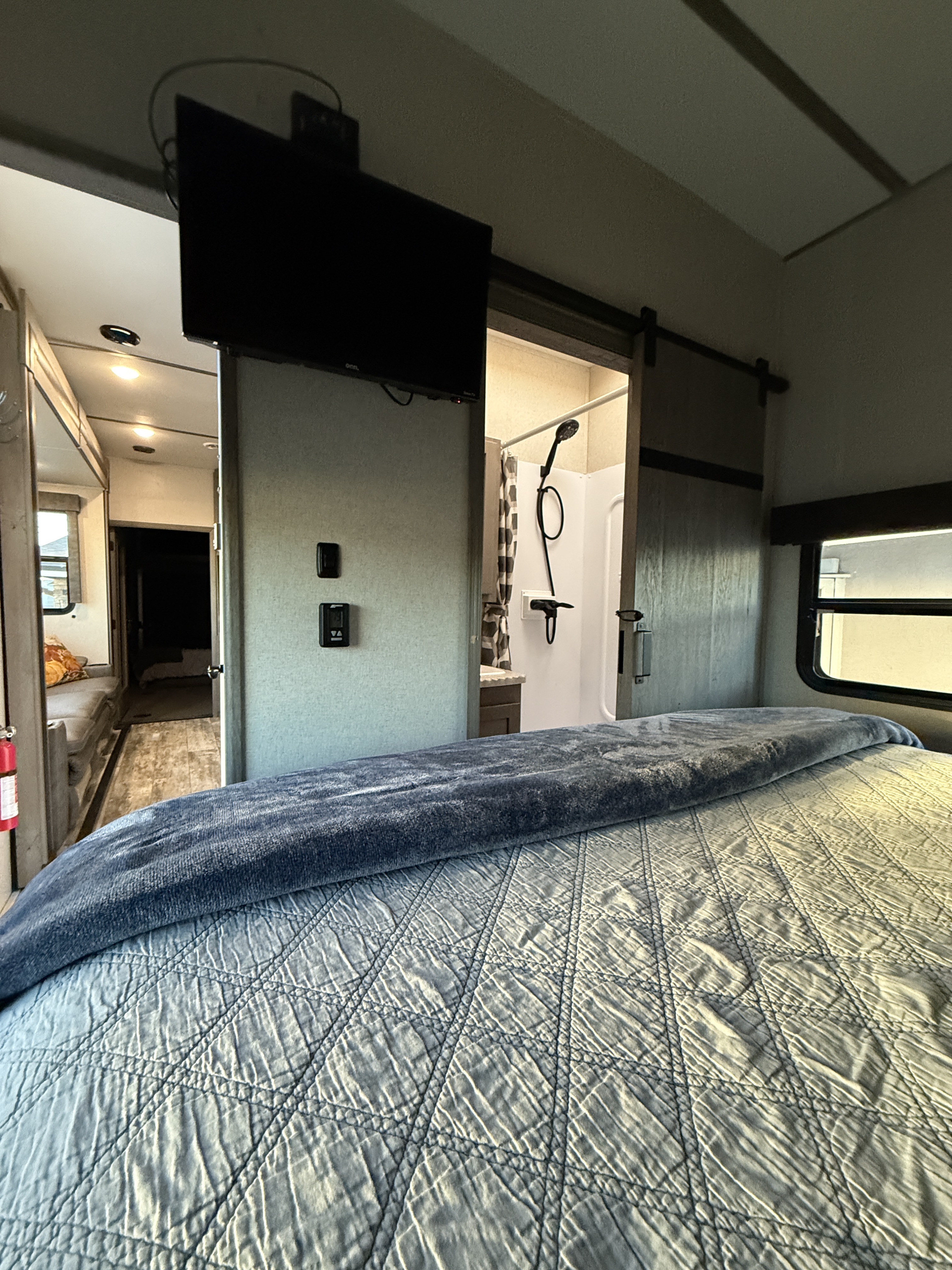 Modern RV rental interior: bedroom with TV, sliding door revealing a shower, and a connected living area.. Keystone Carbon 2021