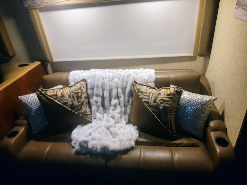 Inside an RV rental: a cozy brown leather sofa with soft white throw, patterned & sparkly pillows, plus cup holders.. Coachman Mirada 2018