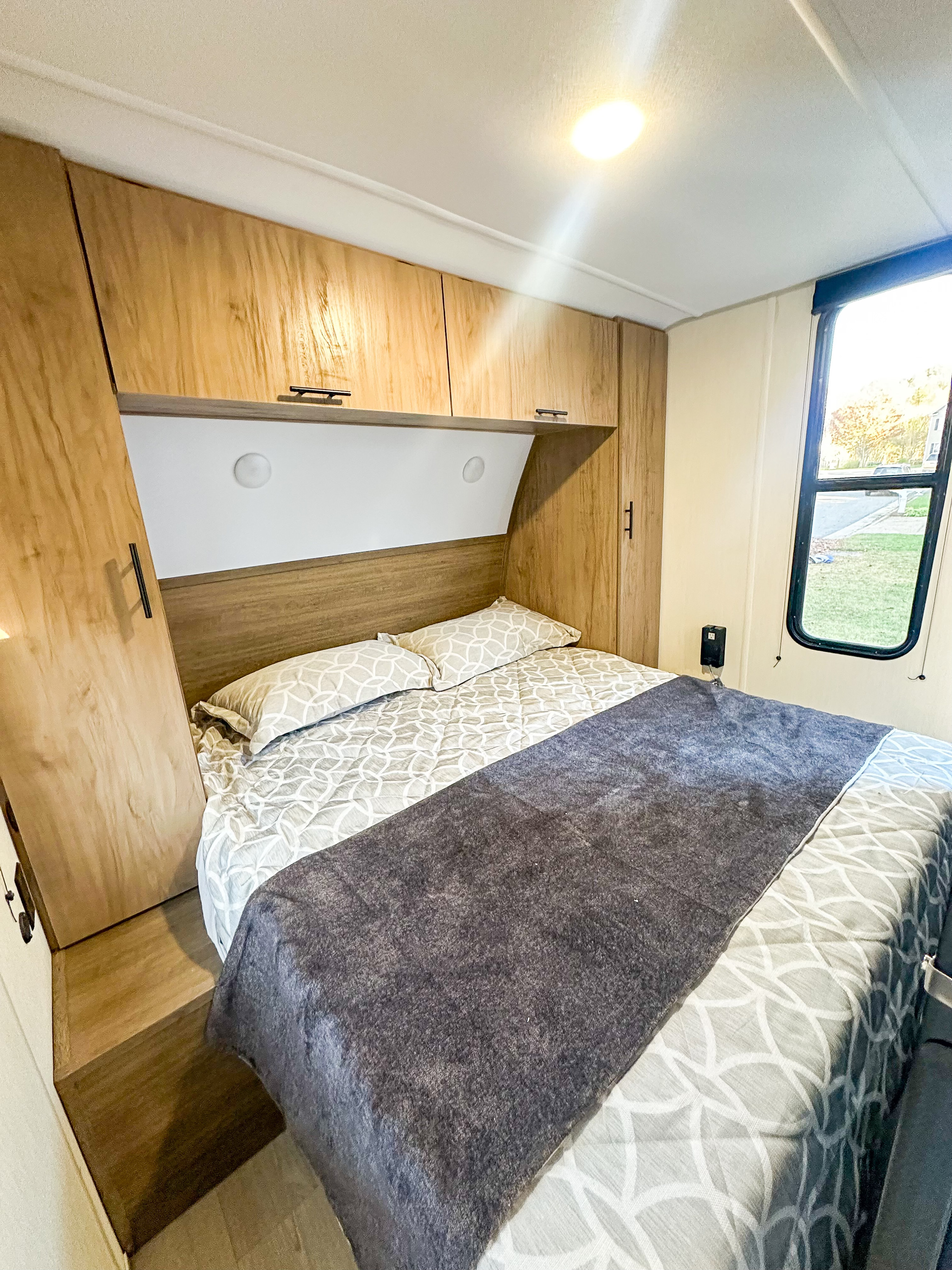 Experience comfort in this RV rental bedroom: light wood cabinetry, a snug bed with geometric bedding, and a large window.. Forest River Grey Wolf 26 DBH 2025