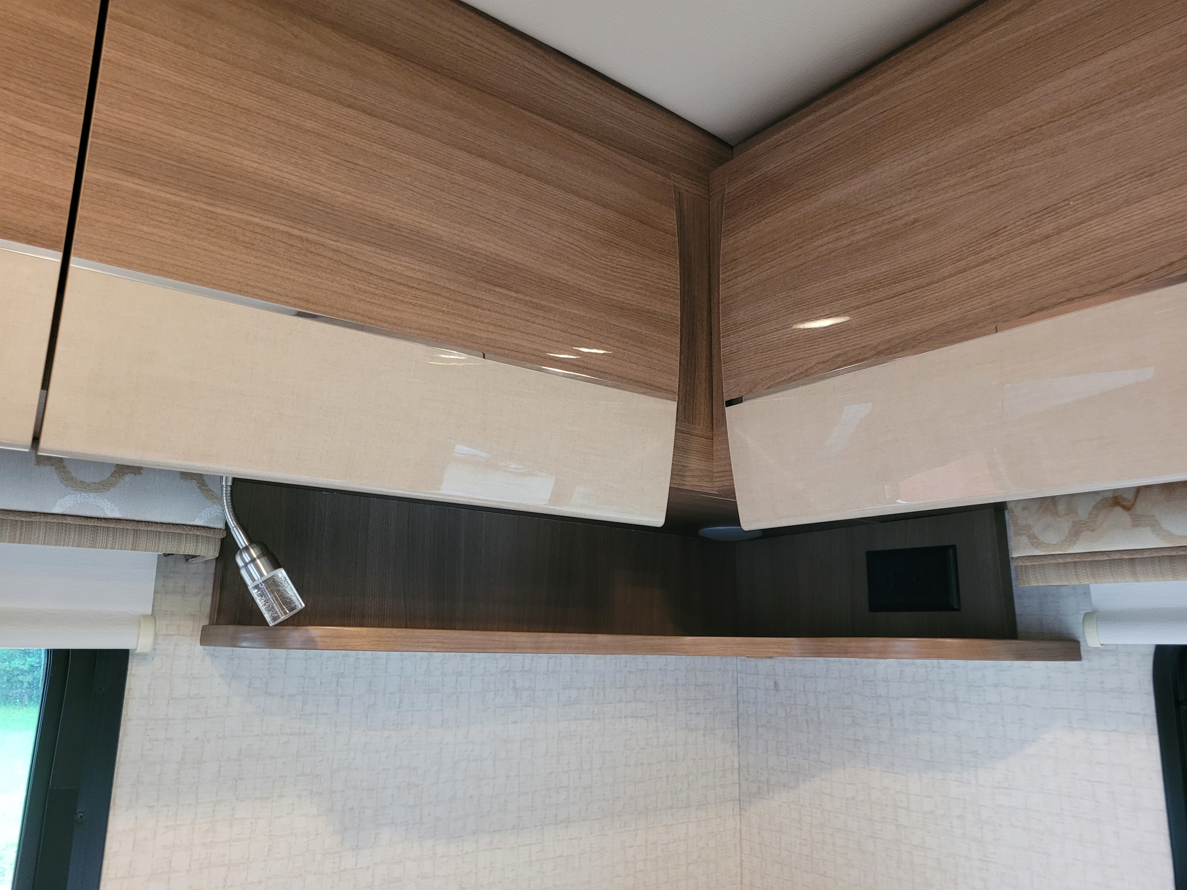 Modern RV rental interior: wood-grain overhead cabinets, light-colored doors slightly open, and a flexible reading lamp.. Winnebago View 2017