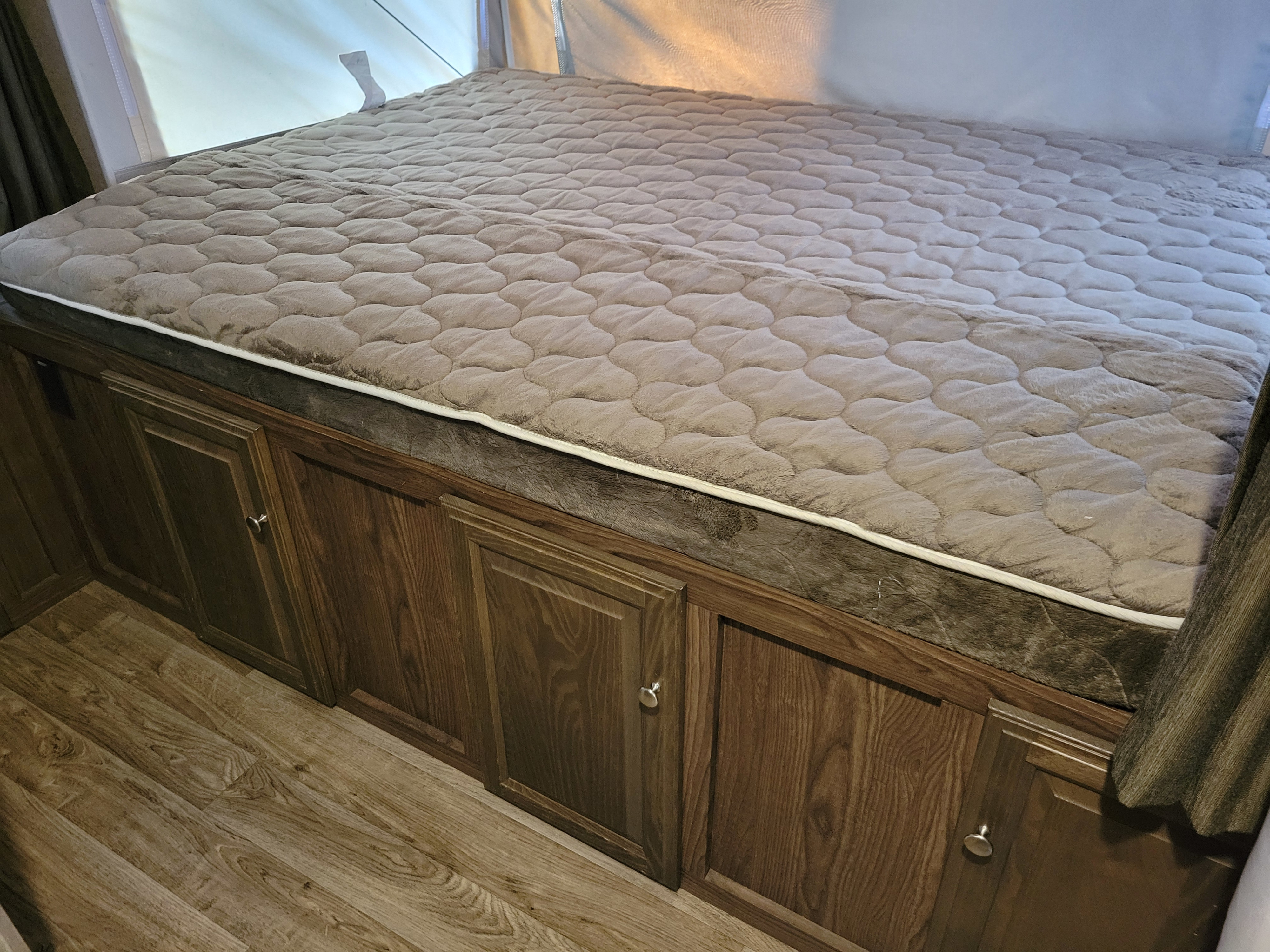 Plush quilted bed in an RV rental, featuring wooden storage cabinets below and laminate flooring. A comfy sleeping area awaits.. Forest River Flagstaff Shamrock 2018