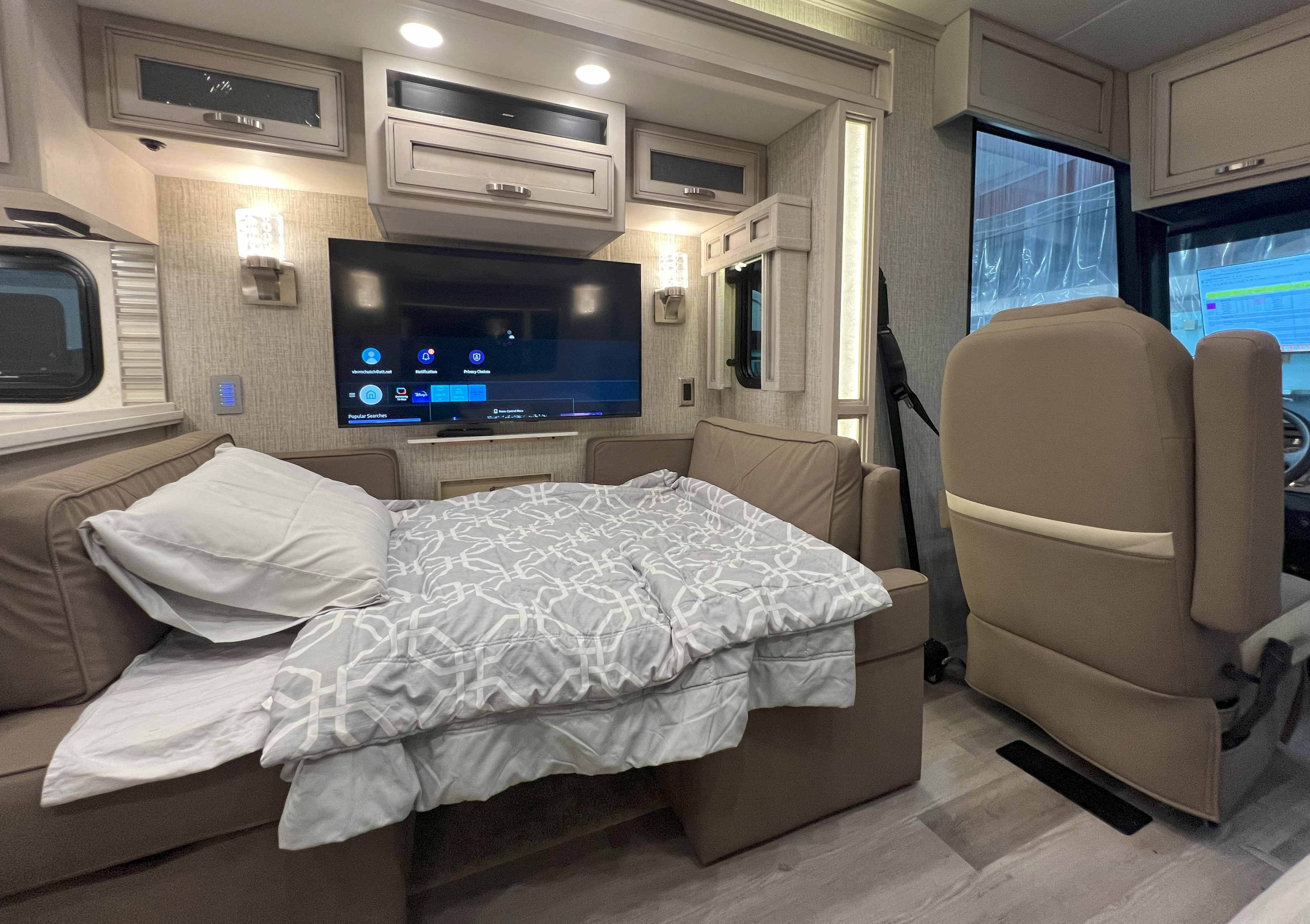 This cozy RV rental interior features a sofa bed with bedding and a large TV, offering a comfortable living and sleeping space.. Holiday Rambler Admiral 2021