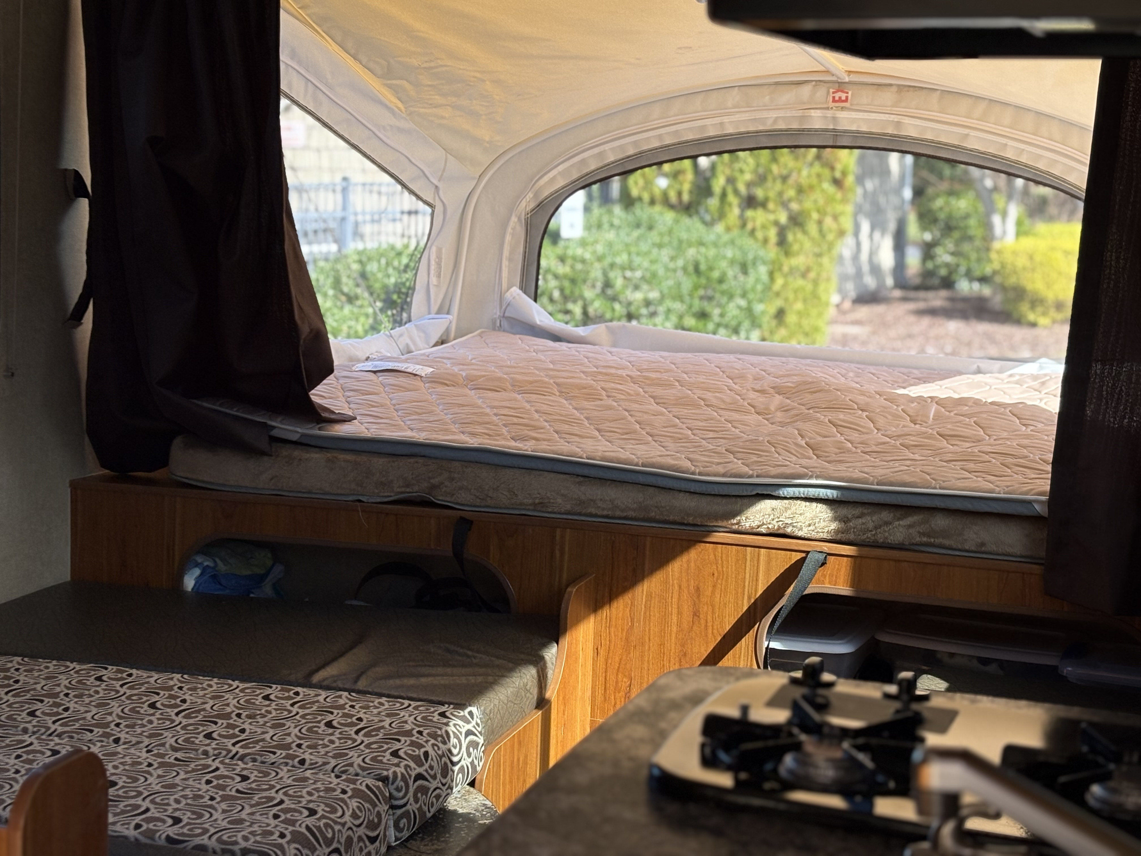 Cozy RV rental interior with a bed, patterned seating, compact kitchen, and bright outdoor view.. Starcraft Launch 2016