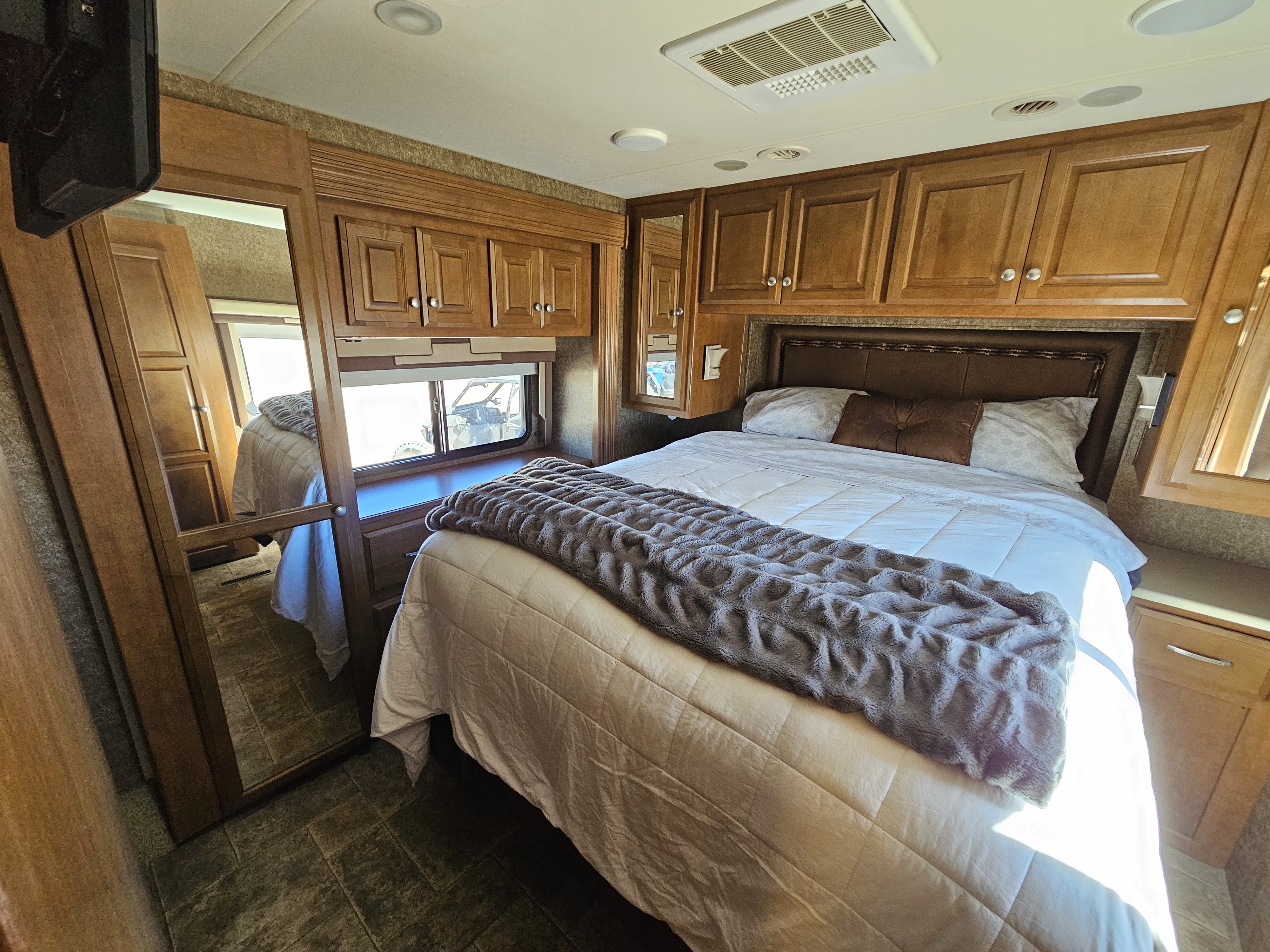 Spacious RV rental bedroom featuring a comfortable bed, wood cabinets, and large window for scenic views.. Thor Palazzo 2013