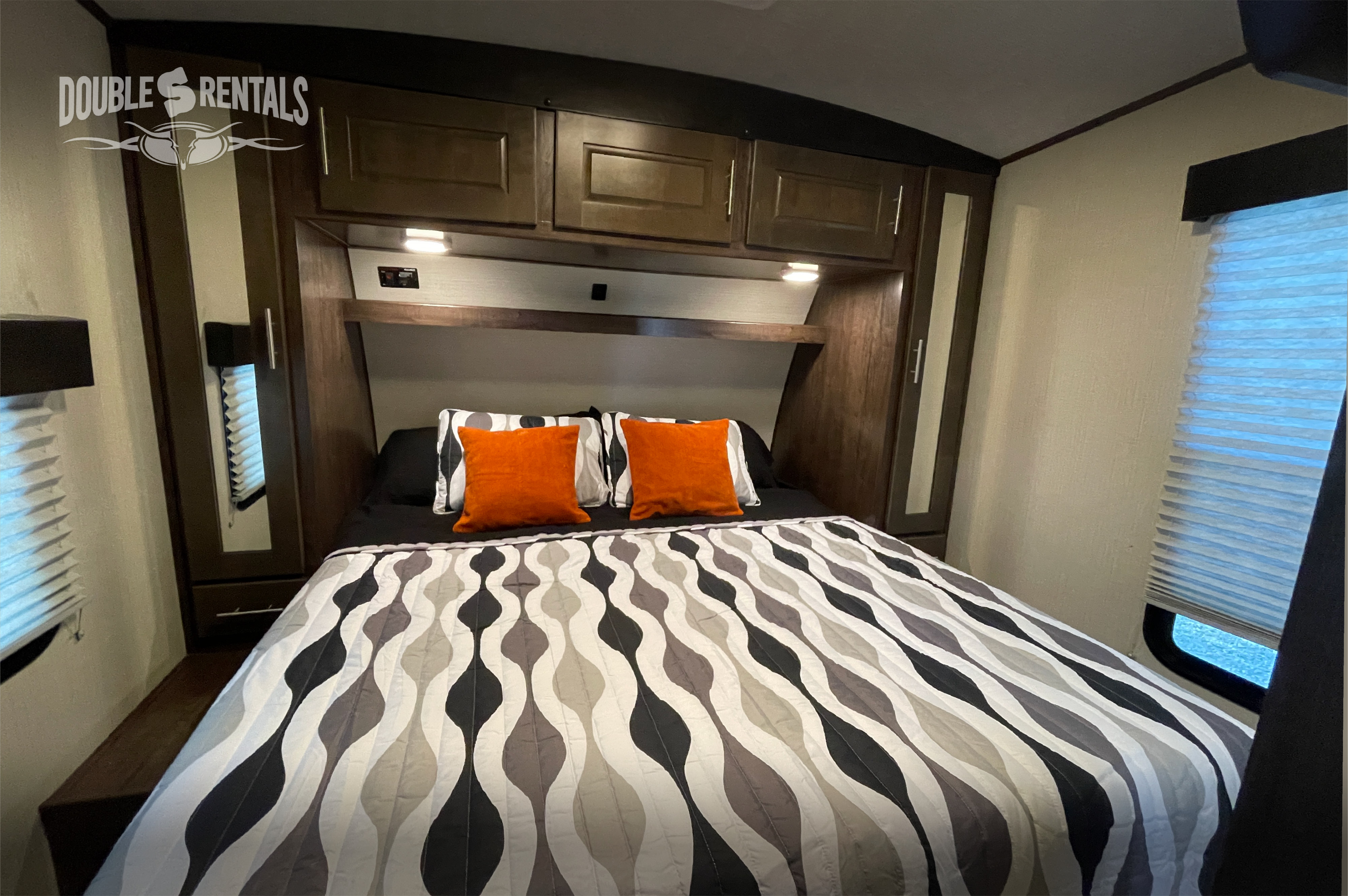 Relax in this comfortable RV rental bedroom, featuring a patterned bedspread, orange pillows, and ample overhead storage.. Heartland Fuel 2020
