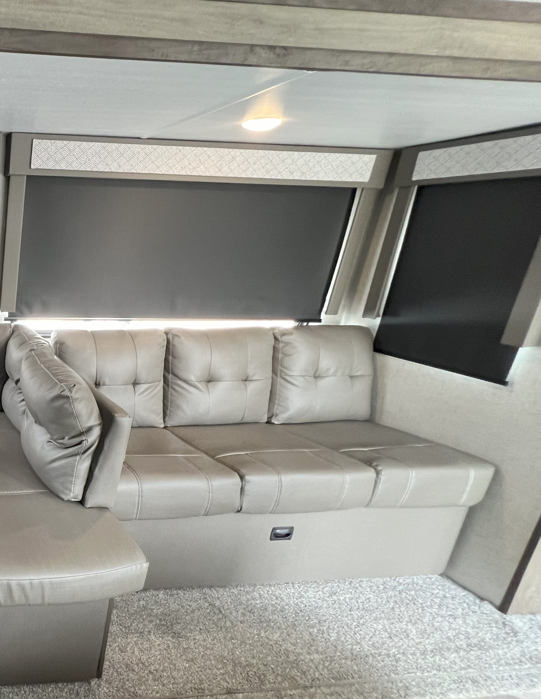 Spacious light-colored L-shaped sofa in an RV rental, featuring dark window blinds, a ceiling light, and carpeted floor.. Forest River Wildwood 2021