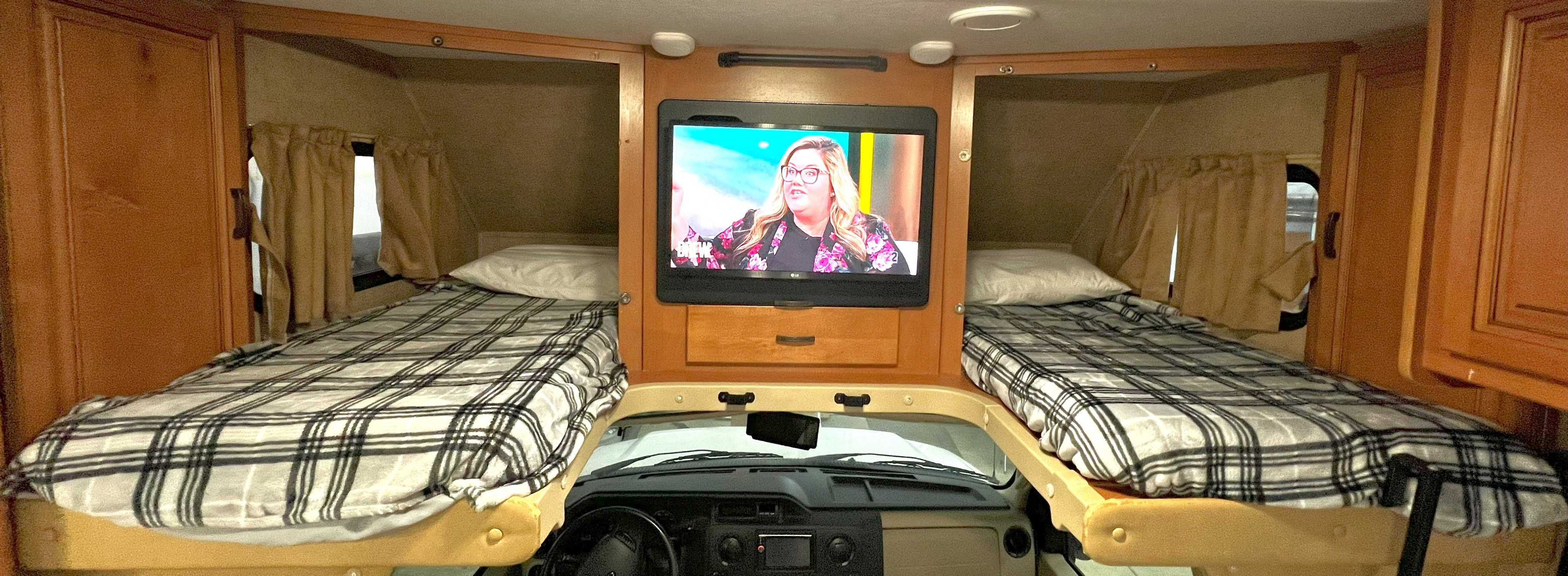 Spacious RV rental interior with twin bunk beds, a mounted TV, and front cab view, ideal for travel.. Forest River Sunseeker 2016