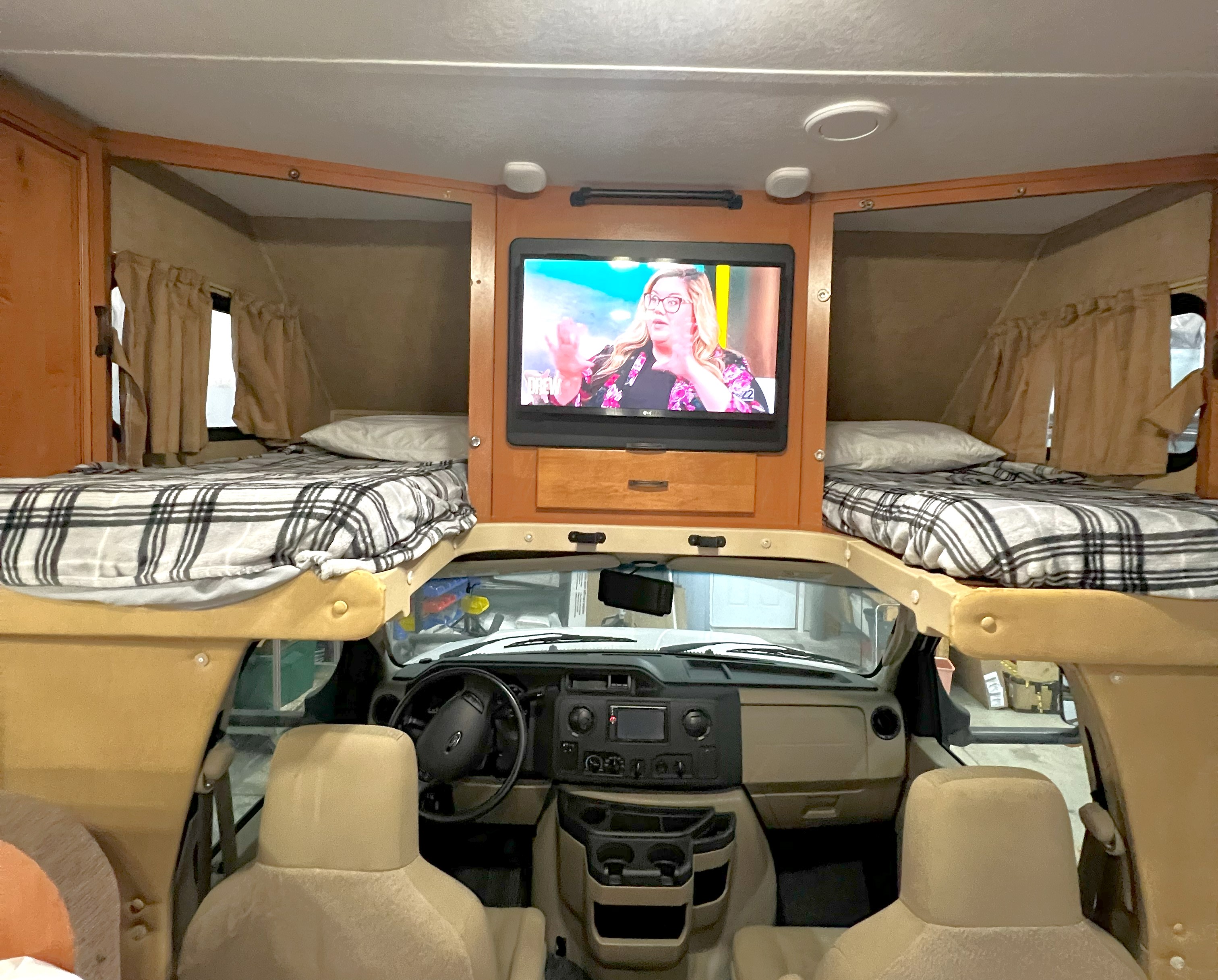 RV rental interior: cozy view with overhead bunk beds, plaid blankets, central TV, and the complete driver's cockpit.. Forest River Sunseeker 2016