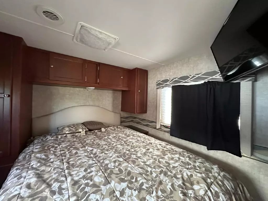 Cozy RV rental bedroom featuring a comfortable bed, ample storage cabinets, and a mounted TV. Ready for your adventure!. Winnebago Minnie Winnie Premier 2014