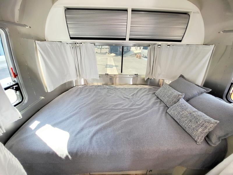 RV rental bedroom: A cozy interior with a queen bed, grey linens, and windows with blinds.. Airstream Bambi 2020