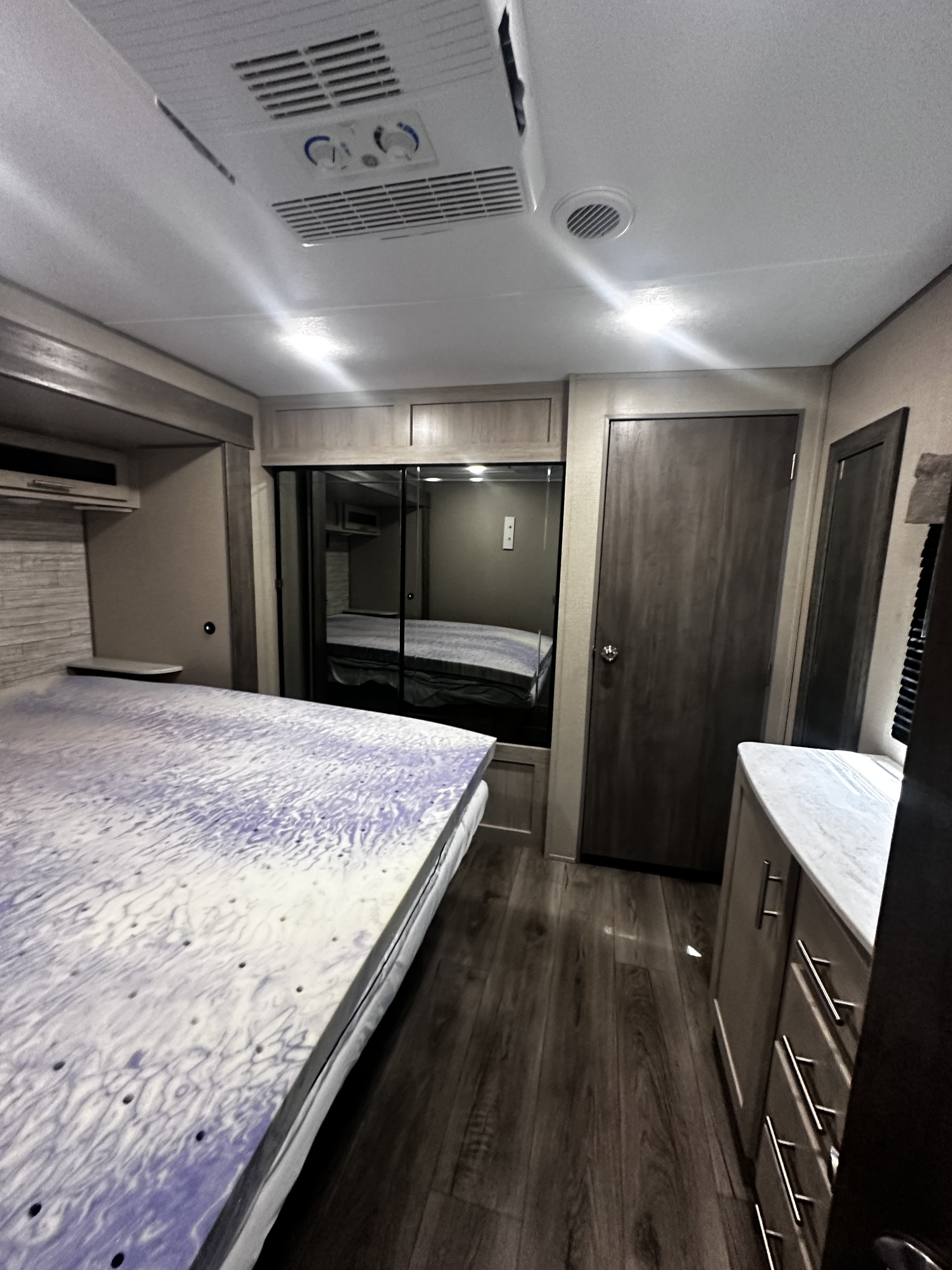 Comfortable RV rental bedroom featuring a large bed with unique topper, mirrored closet, and wood-look floor.. Coachmen 343bhts 2023