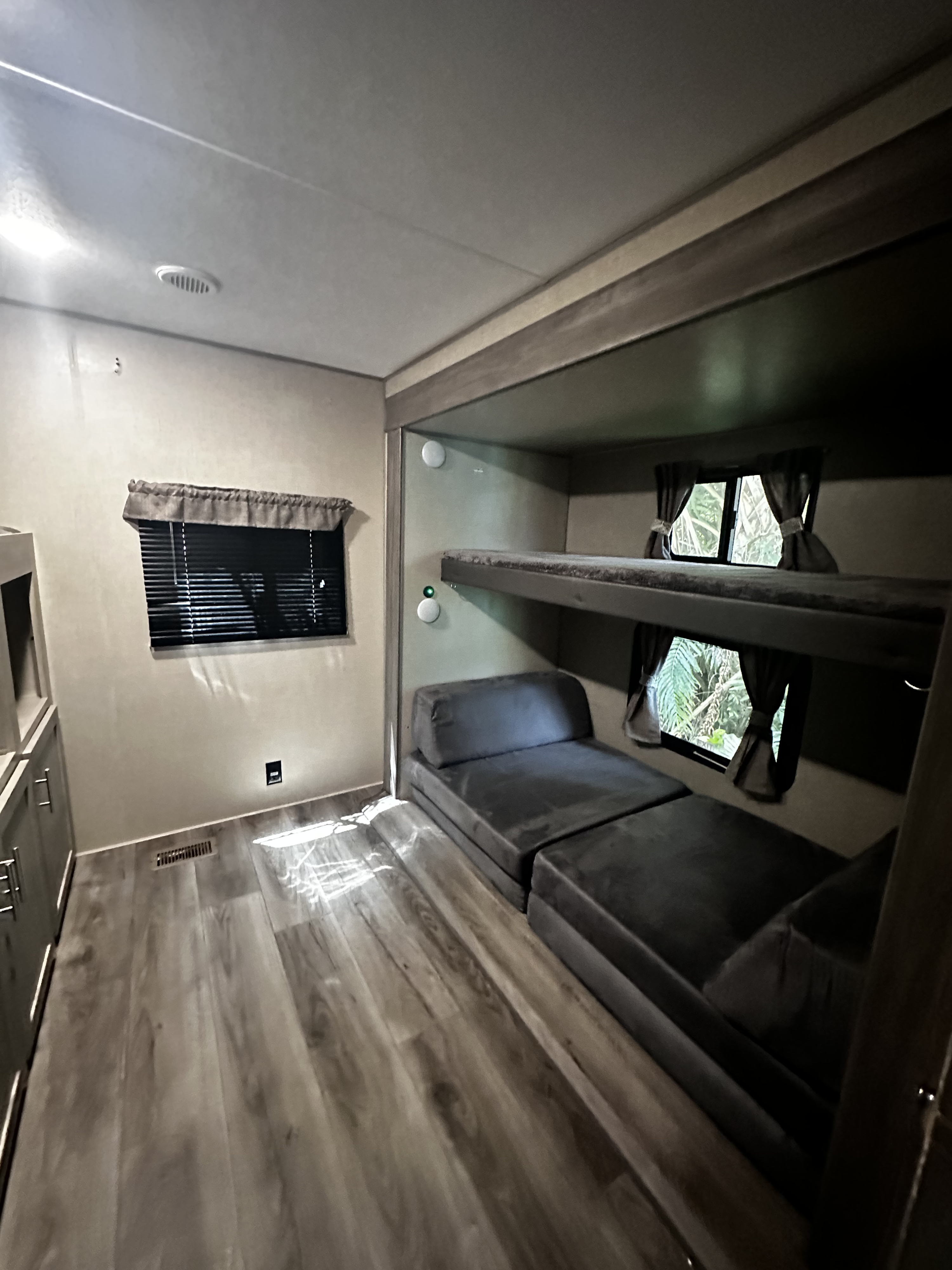 Inside an RV rental: a comfortable bunk bed setup with a lower convertible lounge and bright window views.. Coachmen 343bhts 2023