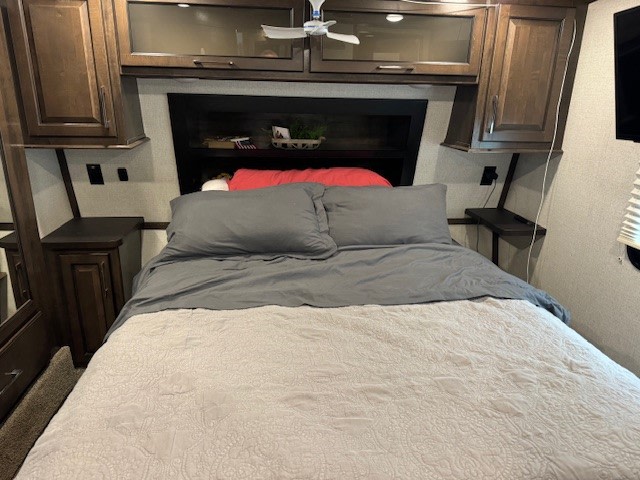 RV rental bedroom: a comfy bed with grey bedding, overhead cabinets, and space-saving side tables for a compact, organized feel.. Dutchmen Voltage 2020