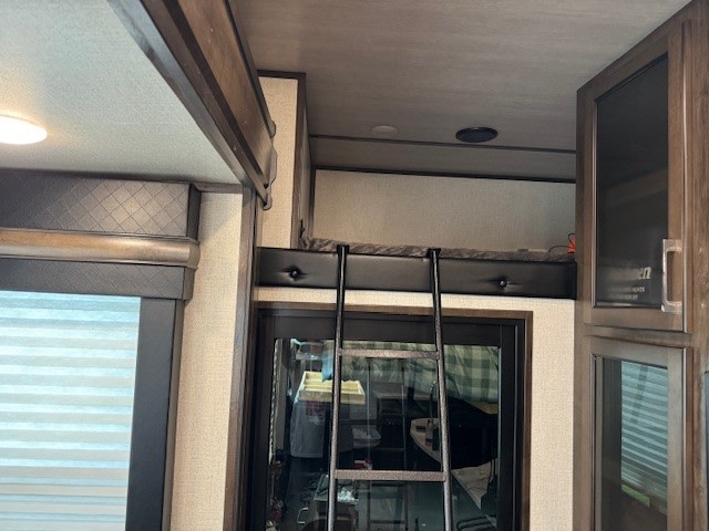 An RV rental interior features a loft sleeping area with a ladder, adjacent wooden cabinets, and a window with blinds.. Dutchmen Voltage 2020