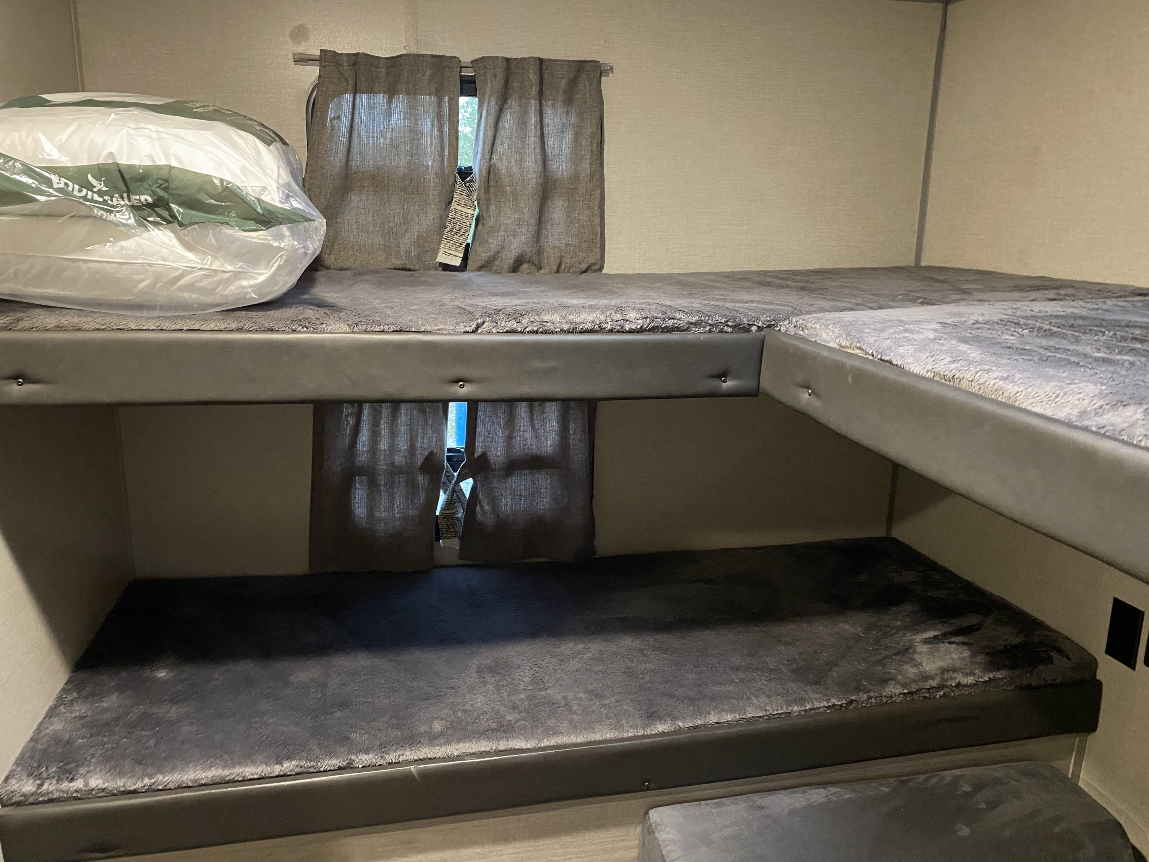 View inside an RV rental showing L-shaped bunk beds with soft grey bedding & curtains, ready for a cozy night's sleep.. Forest River Coachmen Catalina Legacy 2022