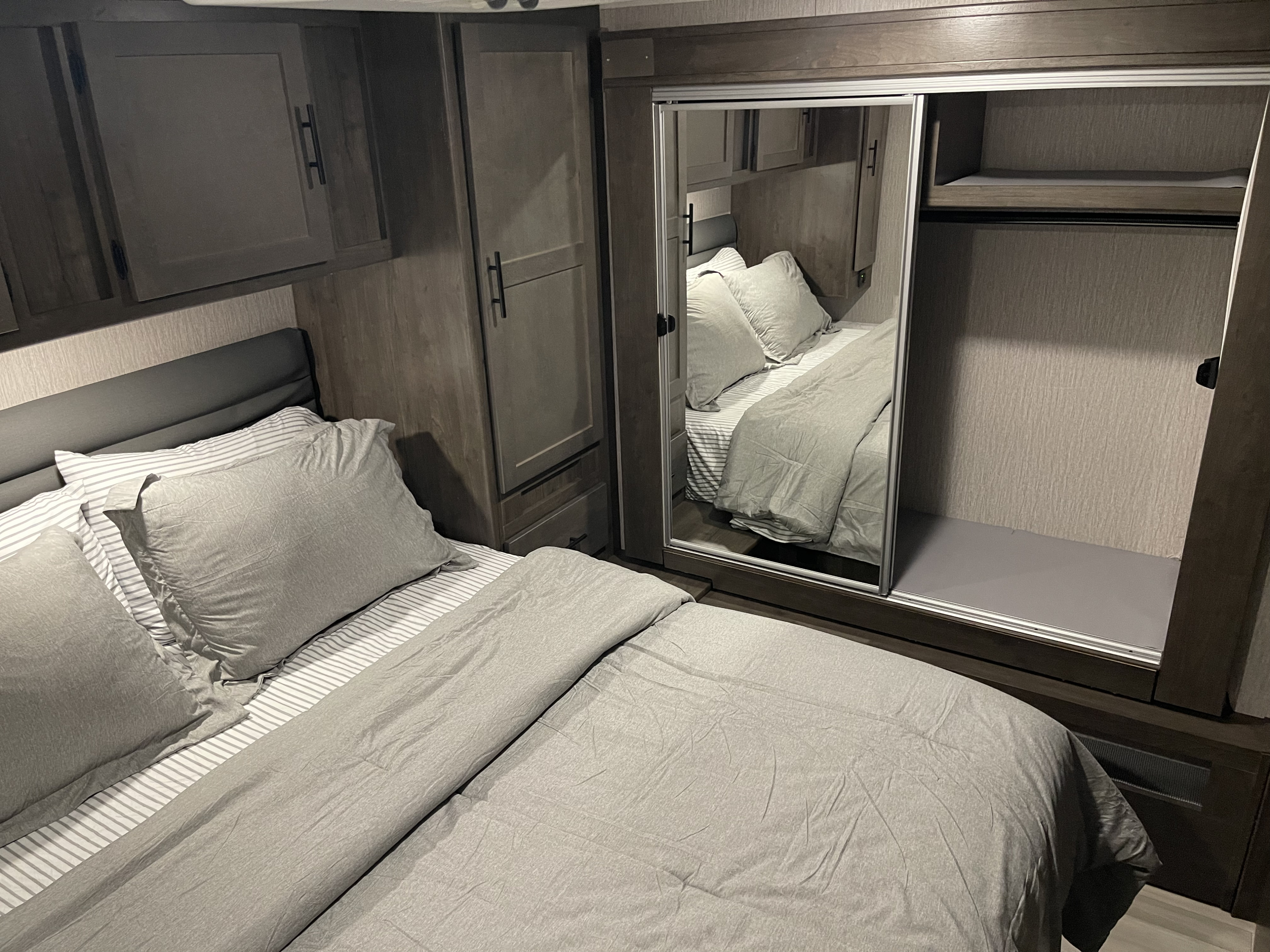 Spacious RV rental bedroom with a comfy bed, modern dark wood cabinetry, and mirrored sliding closet offering ample storage.. Forest River Coachmen Leprechaun Premier 2022
