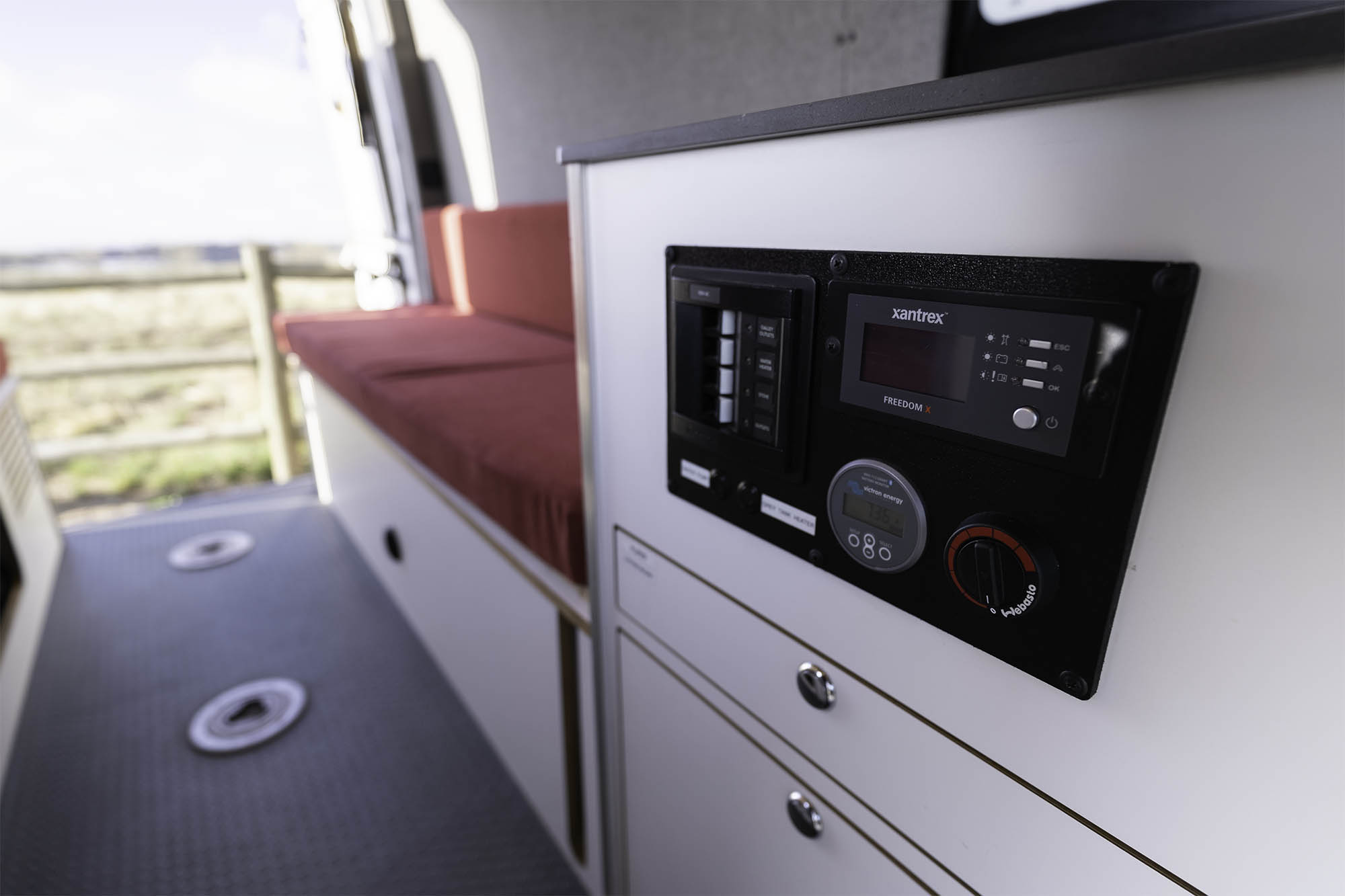 This RV rental offers a detailed control panel: Xantrex inverter, Victron monitor, and Webasto heater. Red bench and storage.. Titan Vans Crestone XL 2020