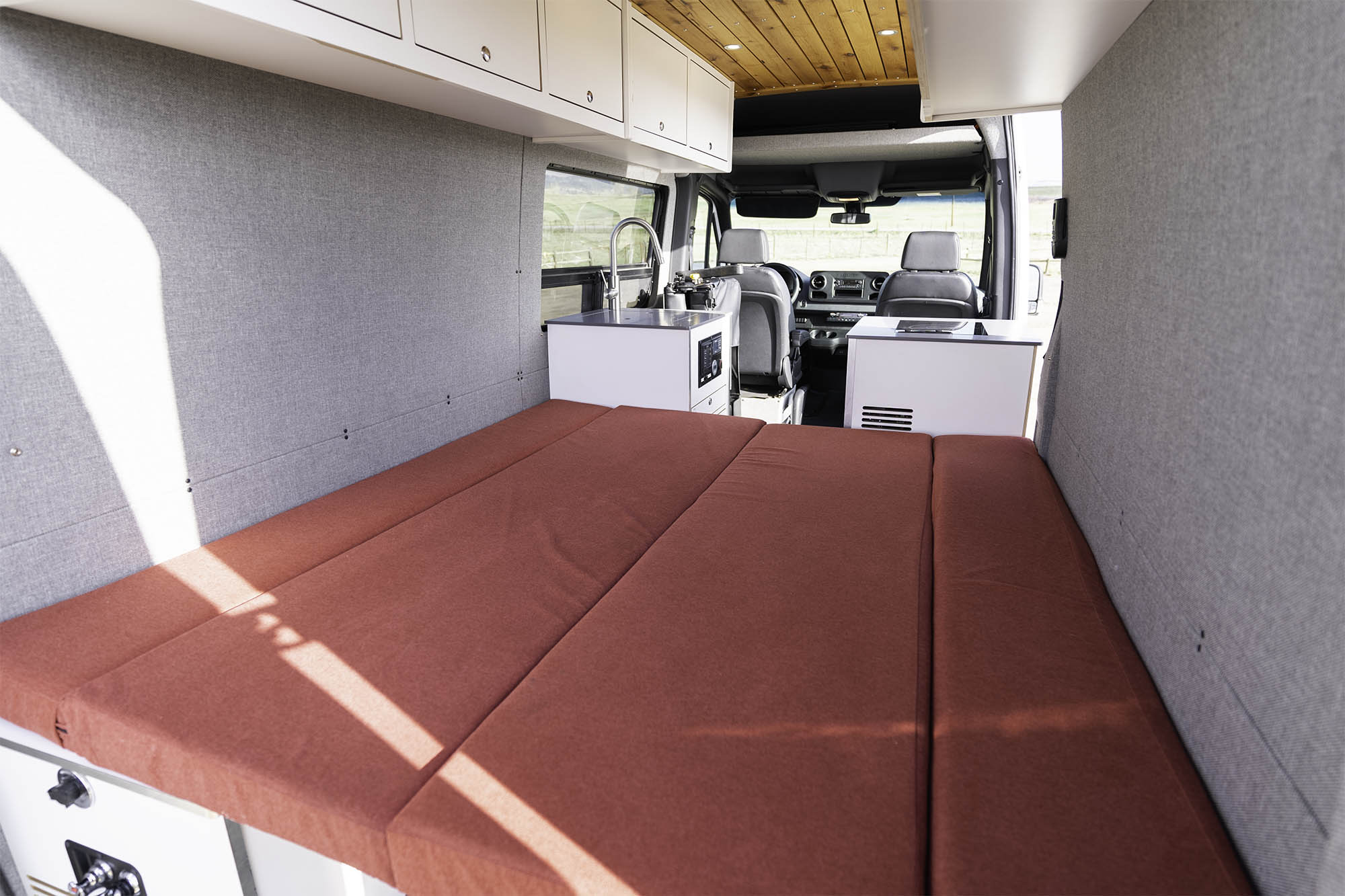 Step into this RV rental, featuring a comfortable red bed, compact kitchen, and ample storage for trips.. Titan Vans Crestone XL 2020