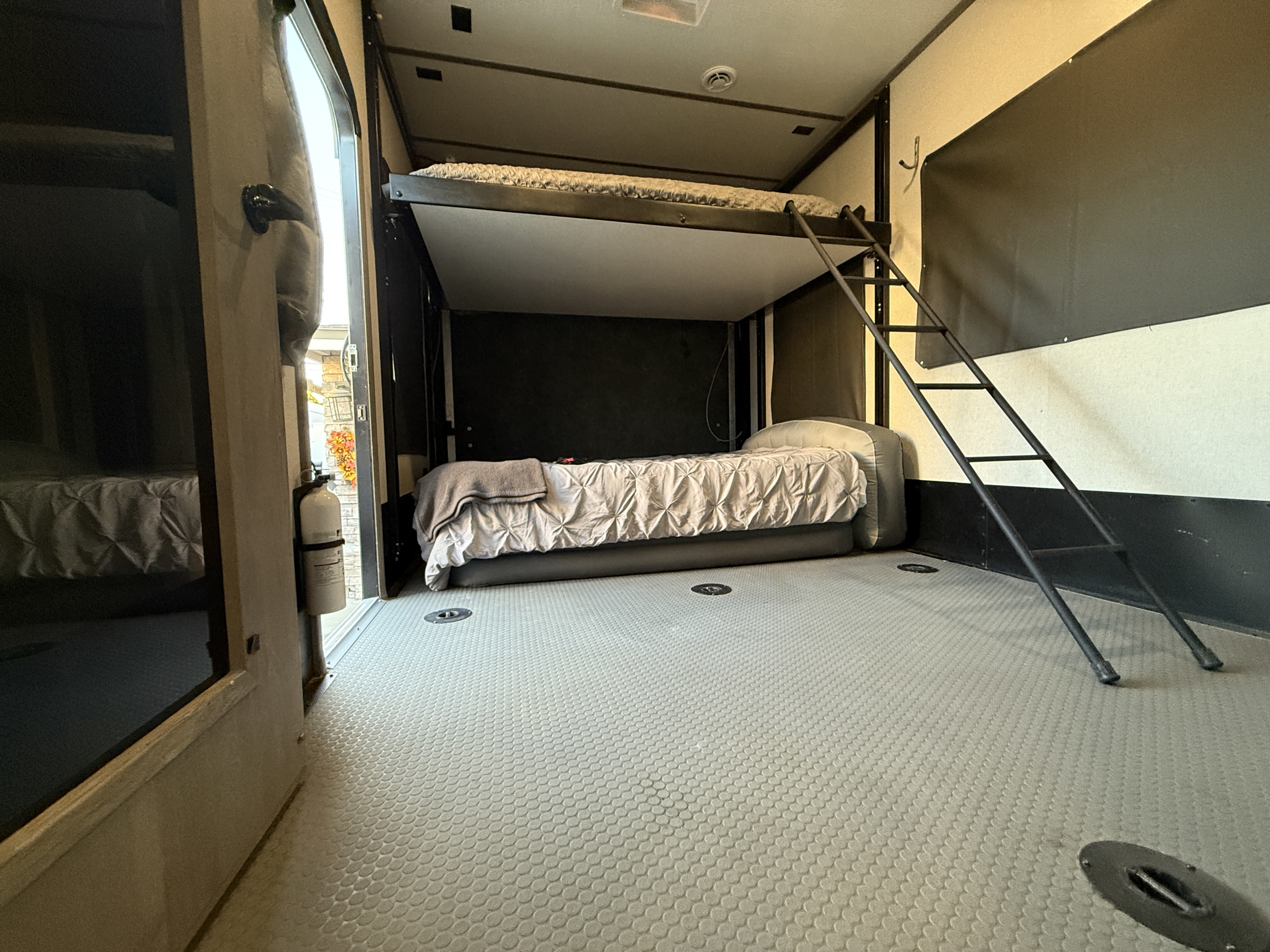 Interior view of an RV rental's sleeping area, showcasing stacked bunk beds, an access ladder, and a durable grey floor.. Keystone Carbon 2021