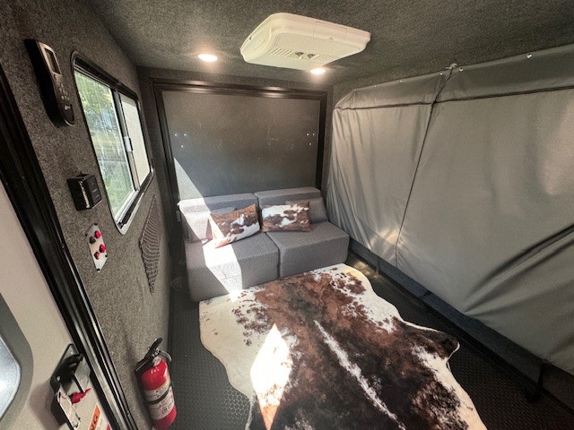 RV rental interior: cozy living space with modular grey sofa, cowhide rug, window, and ceiling AC unit. Fire extinguisher visible.. InTech RV Flyer 2023