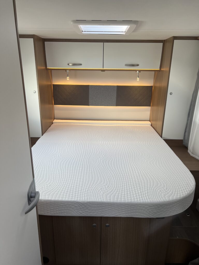 Cozy RV rental bedroom with white mattress, ample storage, and warm lighting, perfect for travel accommodations.. Carado I449 2022