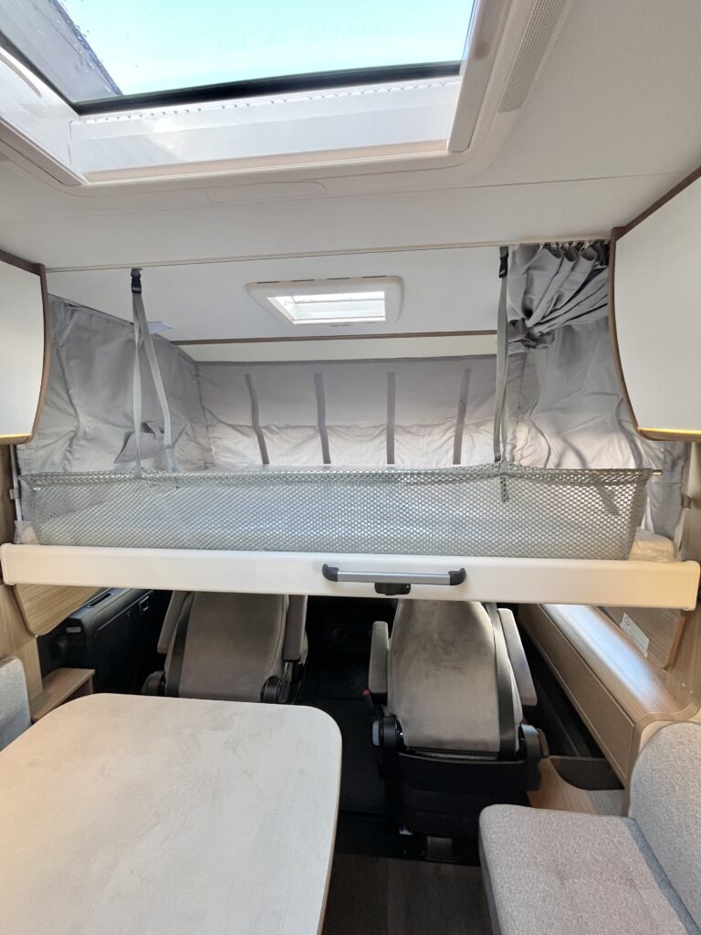 View inside an RV rental showcasing a lowered drop-down bed with safety net, front seats, and dining table.. Carado I449 2022