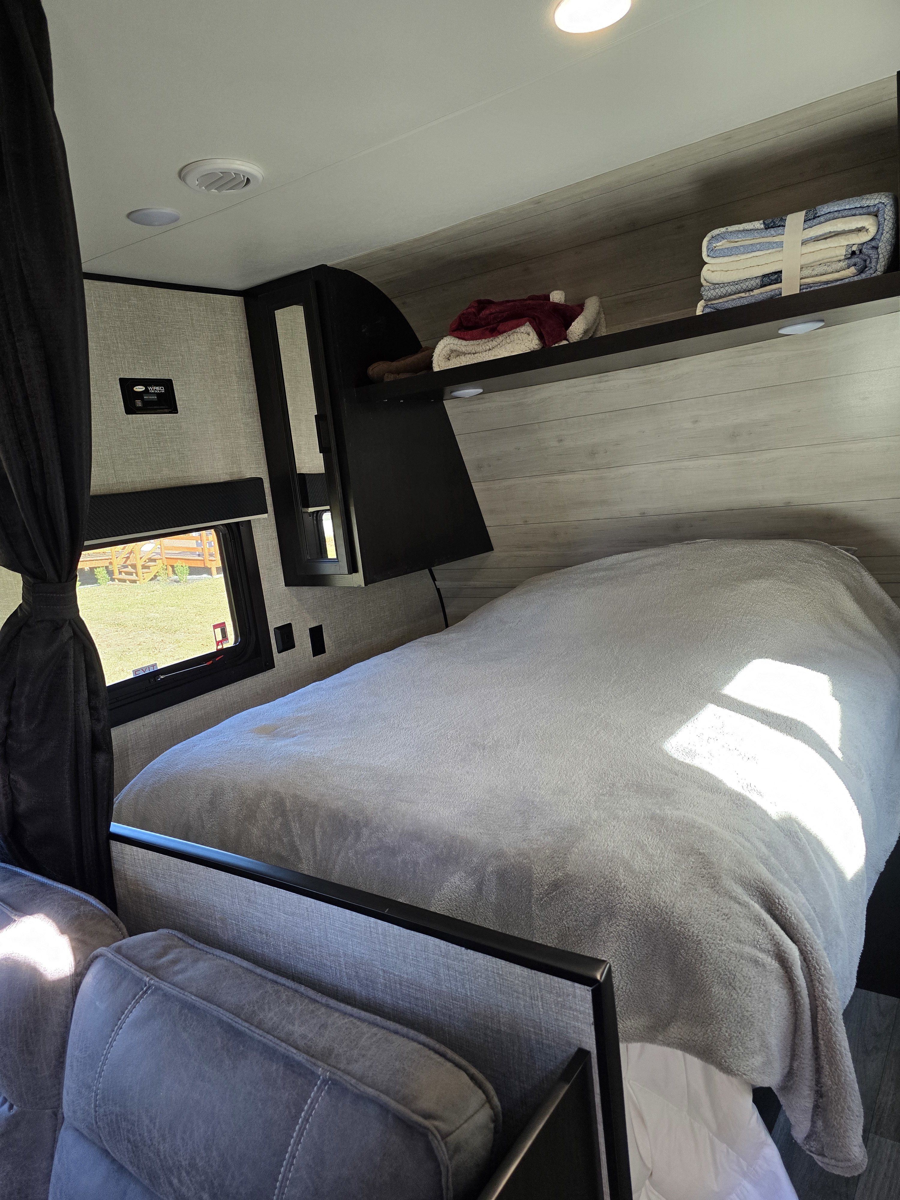 Cozy RV rental bedroom with soft grey blankets, overhead shelves, and a large window.. Jayco Jay Flight SLX 2022