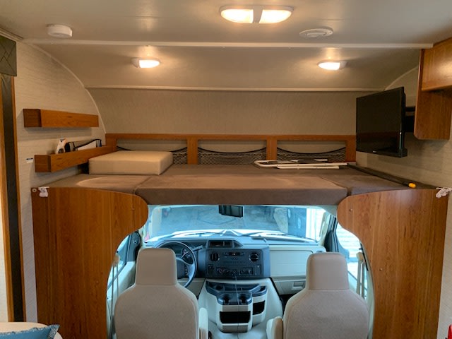 RV rental interior: spacious cab-over bunk bed above the driver's cockpit, with a mounted TV.. Jayco Redhawk 2017