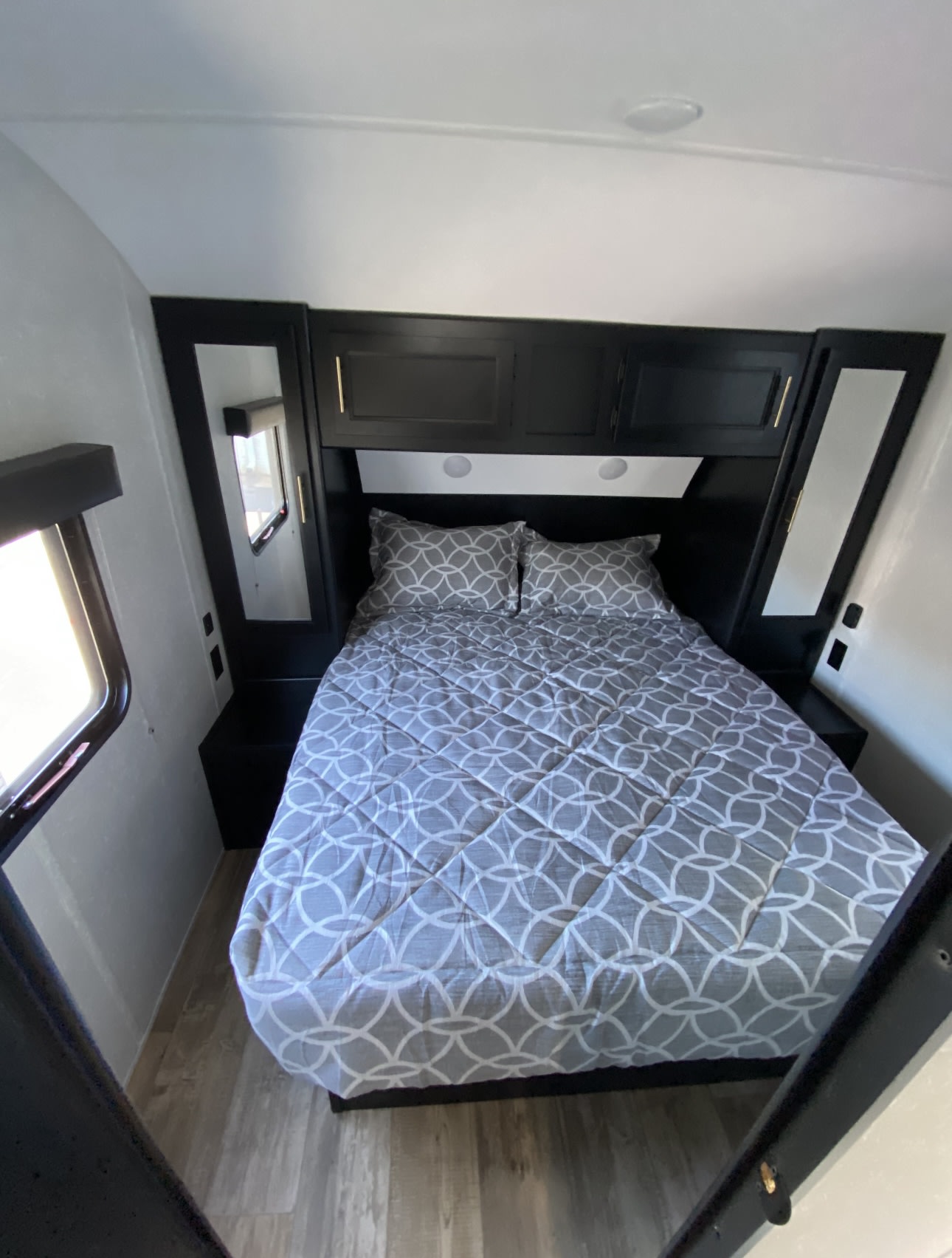 Cozy RV rental bedroom featuring a bed with grey geometric bedding, black built-in headboard, cabinets, and windows.. Forest River Cherokee Grey Wolf 2021