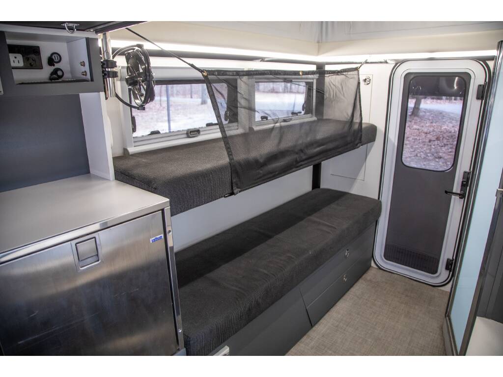 RV rental interior features sturdy bunk beds, safety net, a compact fridge, power outlets, and a door showing trees.. Bruder EXP-6 2018