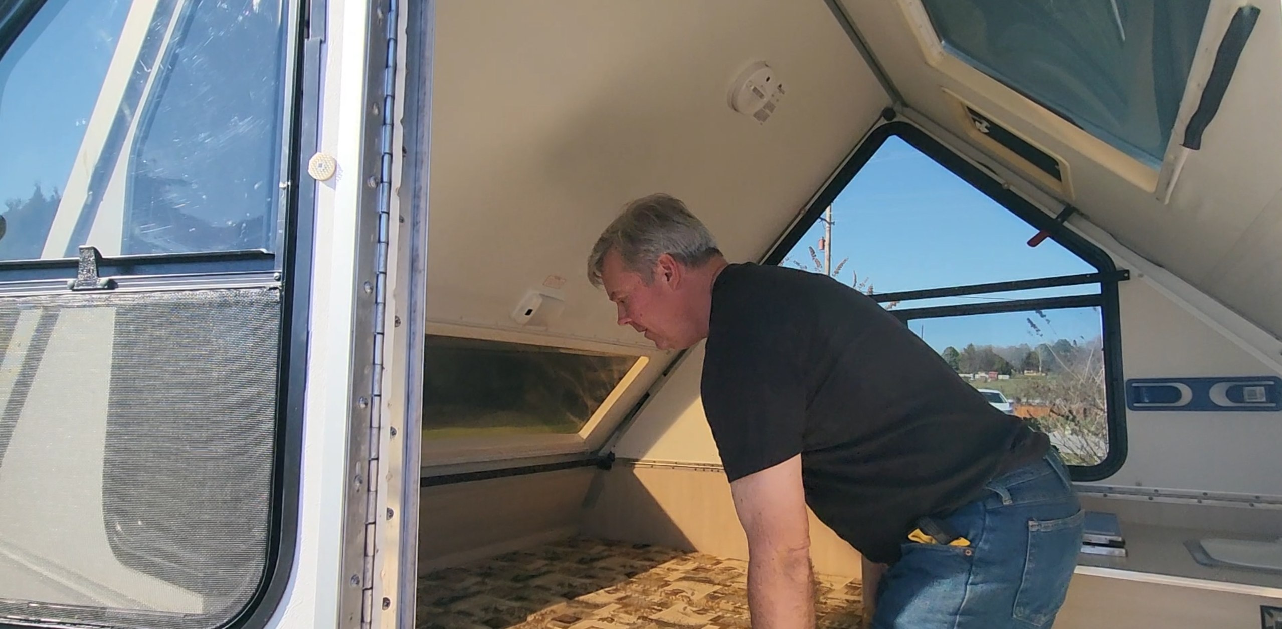Man leans into an A-frame RV rental, inspecting its light interior. The compact camper features a bed area and numerous windows.. A Liner A Liner Popup Trailer 2006