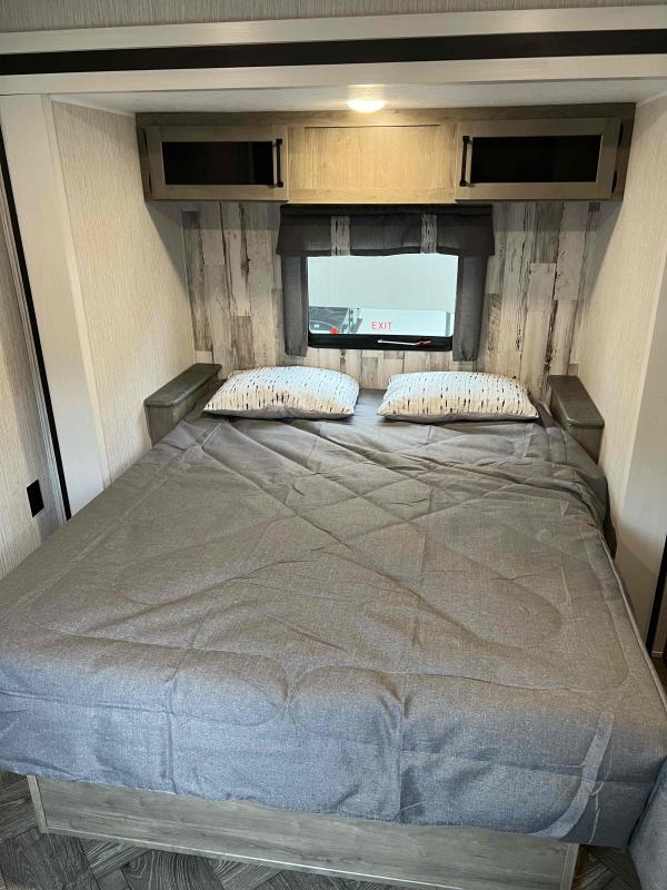 Inside an RV rental: a cozy bedroom with a large bed, overhead cabinets, and a window displaying 'EXIT'.. Palomino Puma 2022