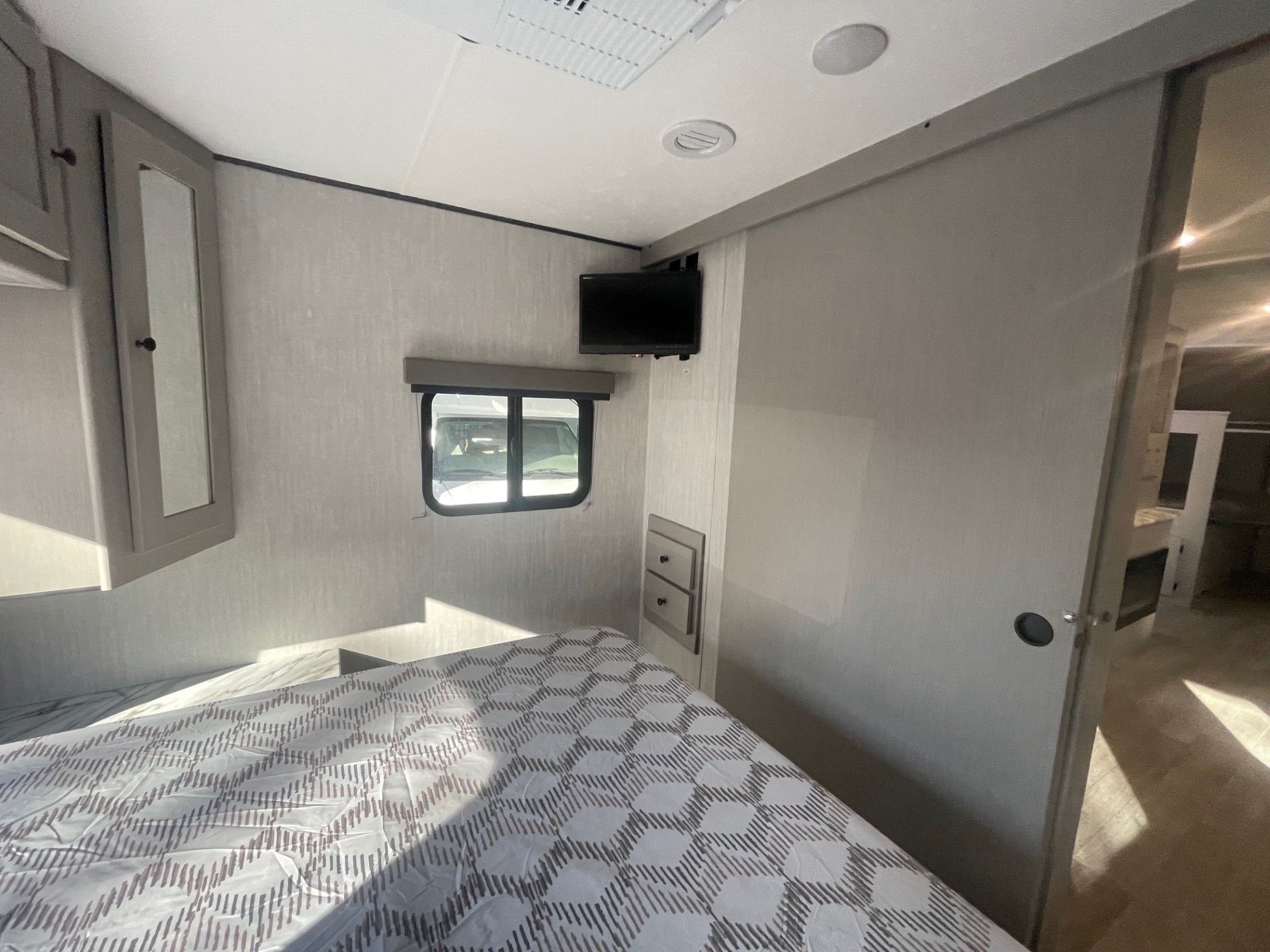 Bright RV rental bedroom: Features a large bed with patterned comforter, wall-mounted TV, window, and cabinetry.. Coachmen APEX 284BHSS 2025