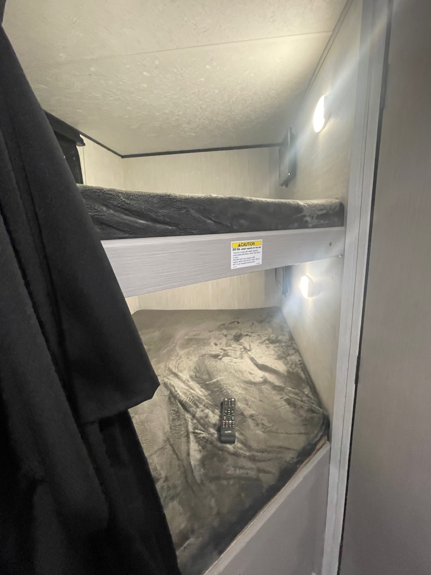 This RV rental features compact bunk beds, each with its own light. A remote rests on the lower bed.. Coachmen Apex 245 BHS 2025