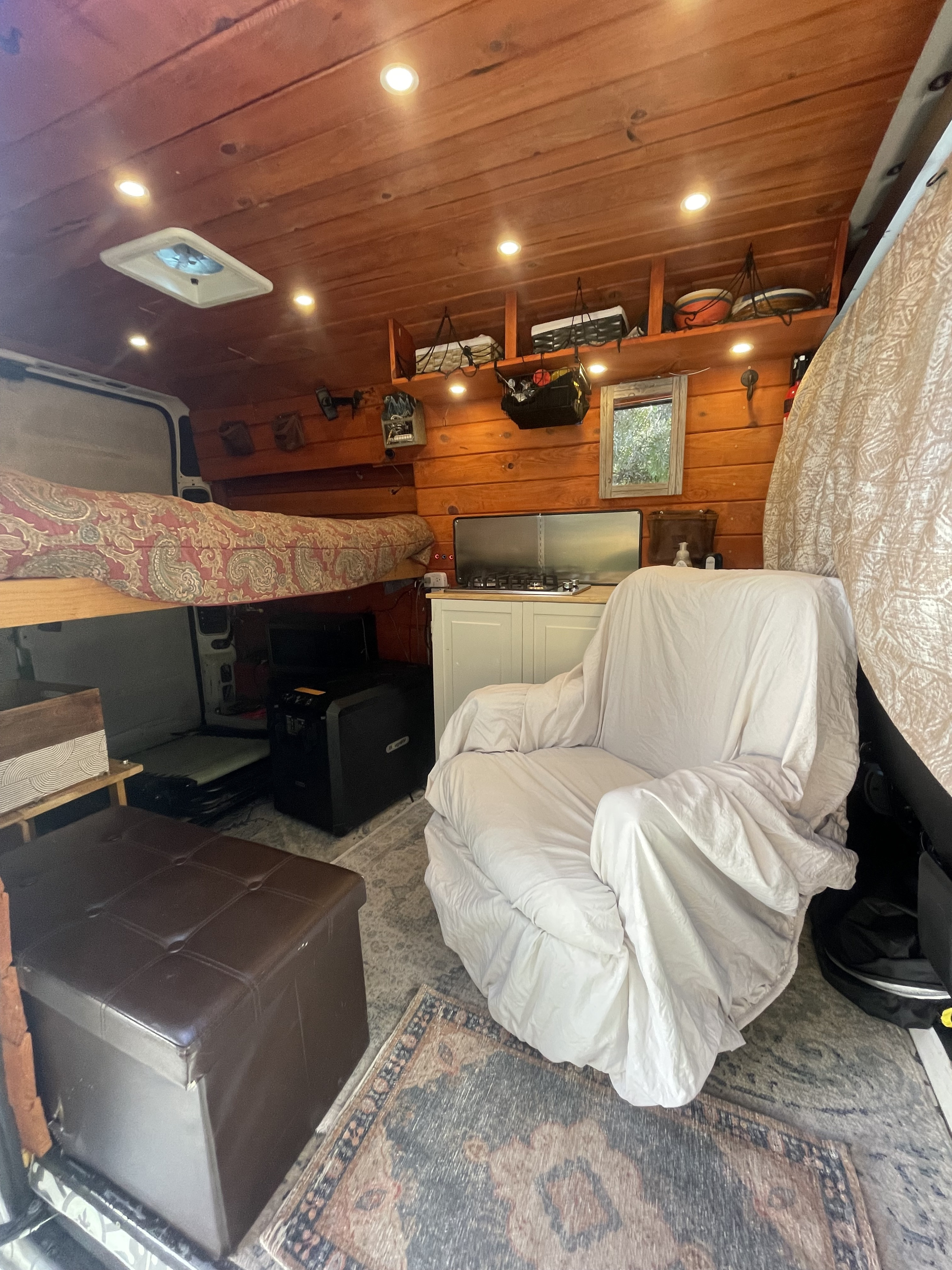 Cozy RV rental interior: wood-paneled walls, raised bed, kitchenette, and a comfy armchair.. Dodge Other 2021