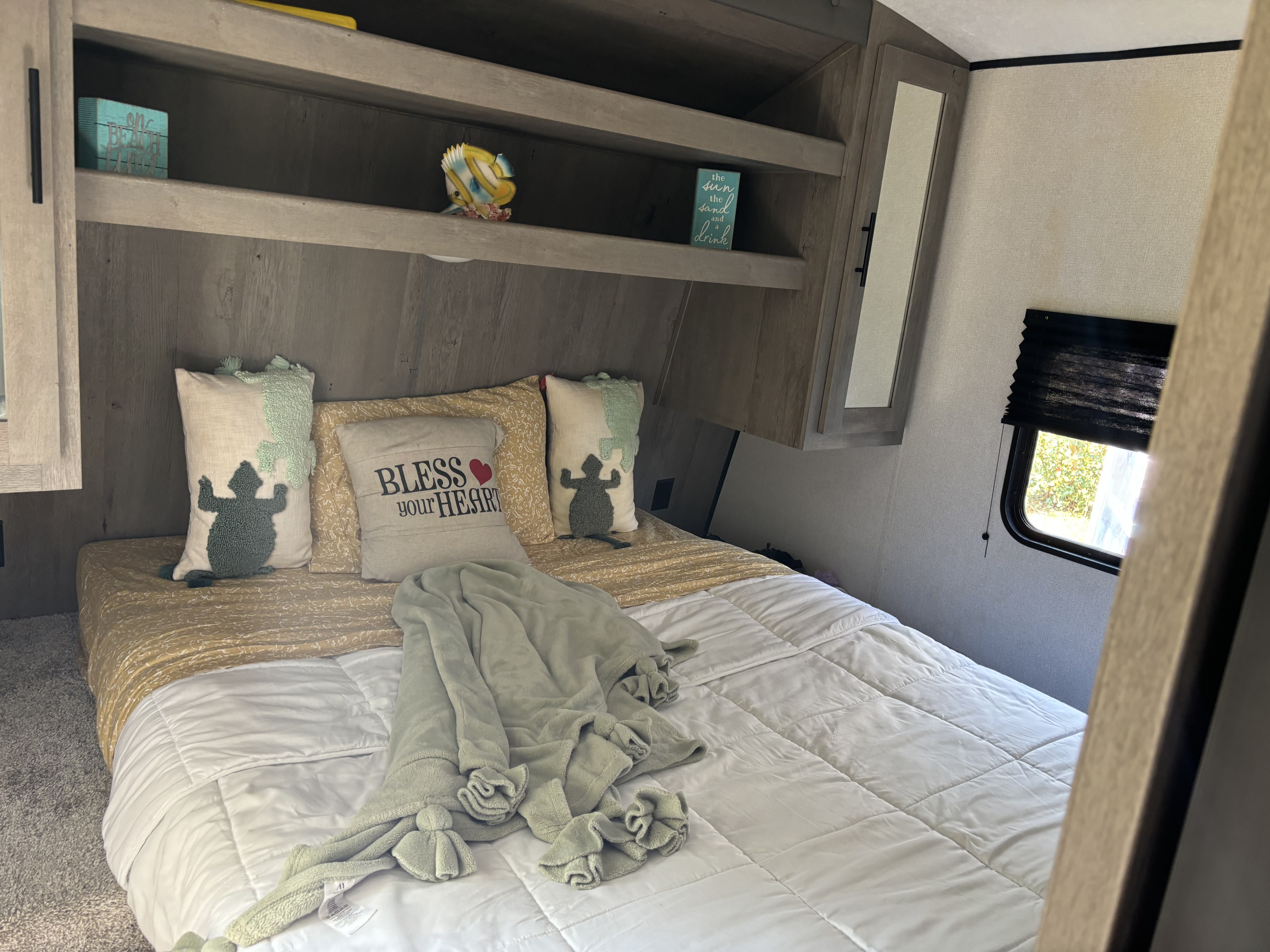 Relax in this charming RV rental bedroom featuring a comfy bed, turtle pillows, beach-themed decor, and shelves.. Keystone RV Springdale 2021