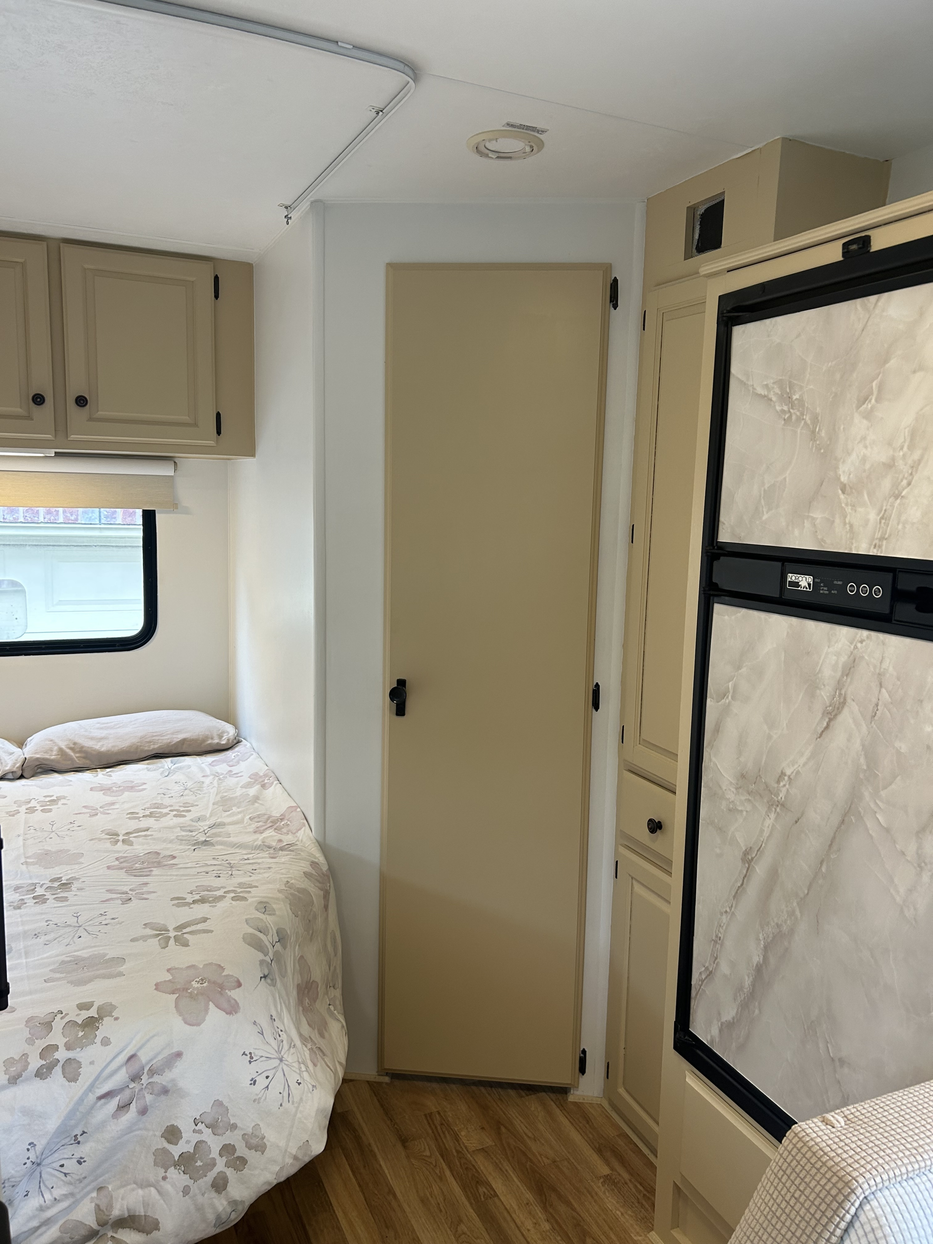 RV rental interior: cozy bedroom with floral bedding, leading to a door and kitchen area with a Norcold refrigerator.. Ford Ford E350 1997