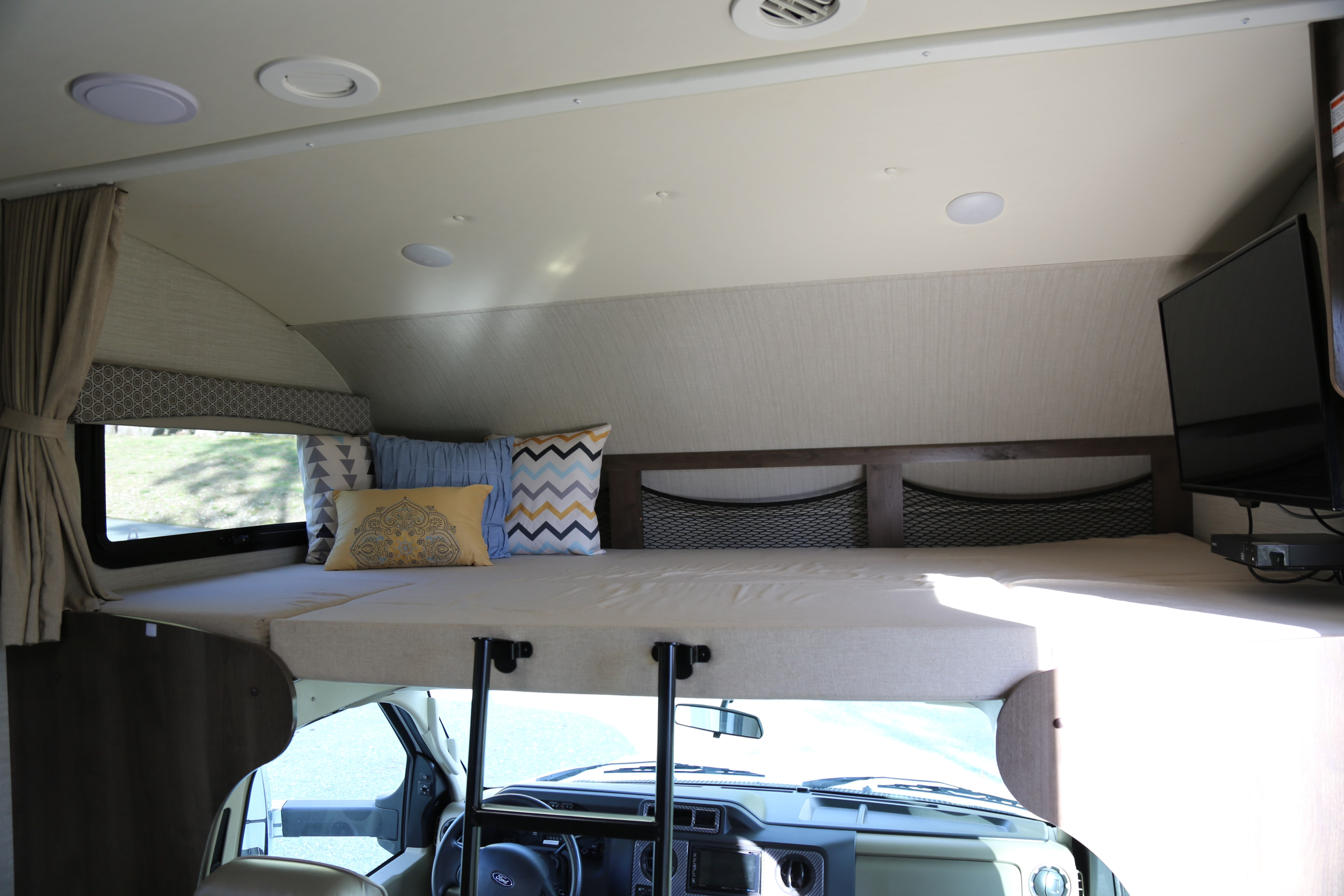 RV rental: Overhead bunk bed with pillows, window, storage nets, and TV for a cozy stay. Driver's cab visible below.. Jayco Greyhawk 2019