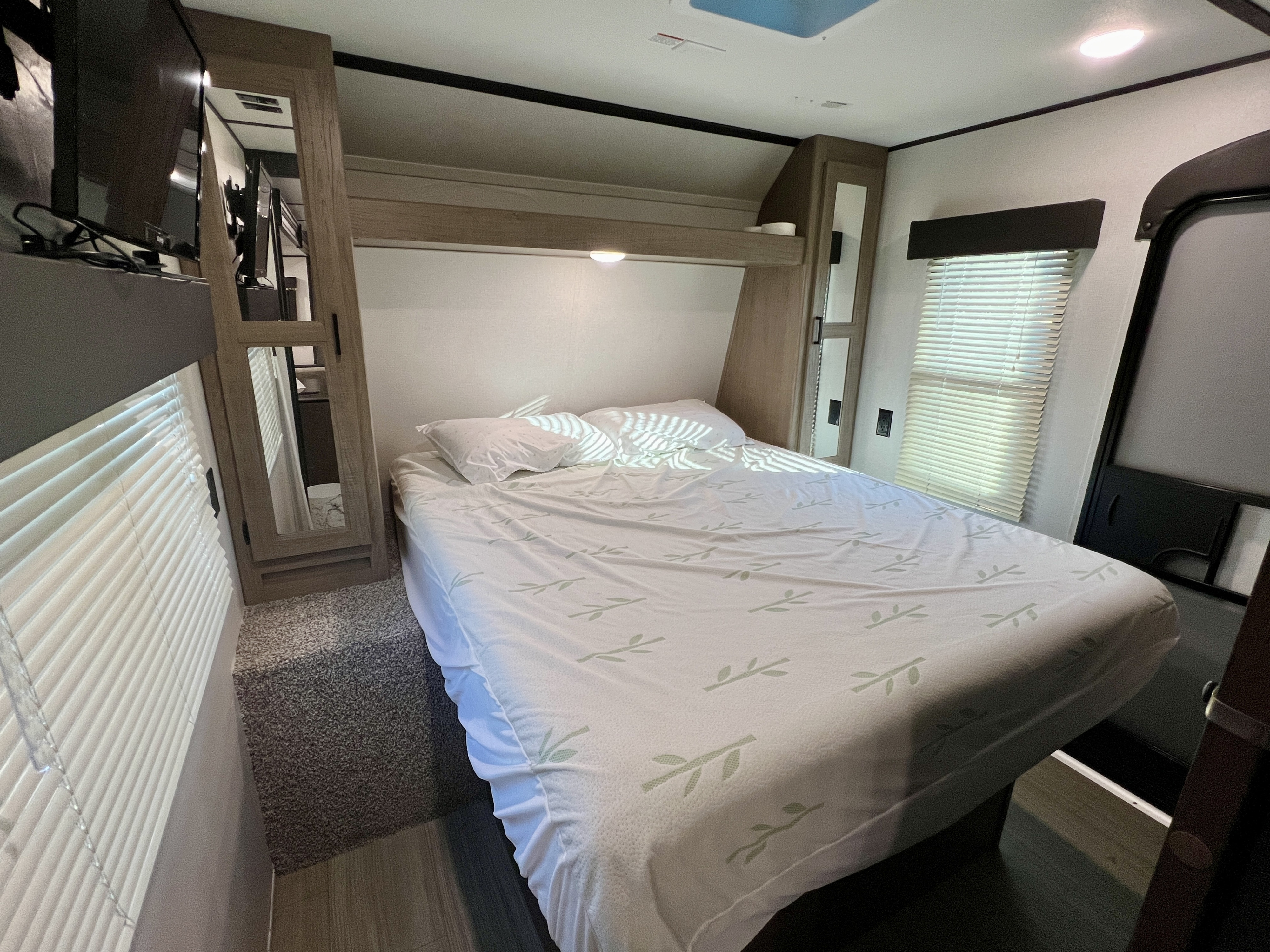 RV rental interior showing a compact bedroom with a comfortable bed, mirrored storage, and TV.. Keystone Hideout 2020
