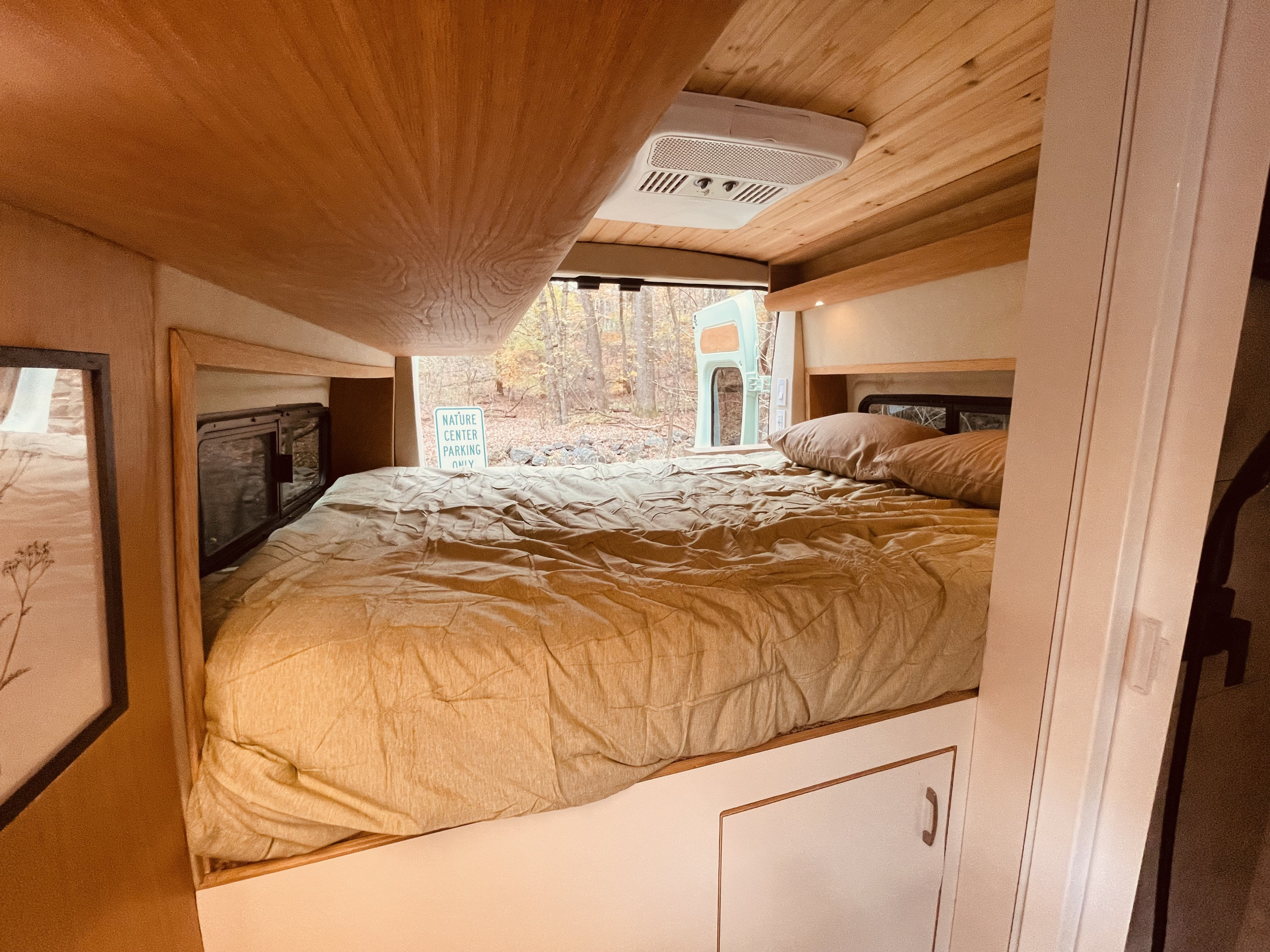 Cozy RV rental sleeping area with a comfortable bed, wood interior, and nature views from the back.. Dodge Pro Master High Roof 3500 Extended 2021