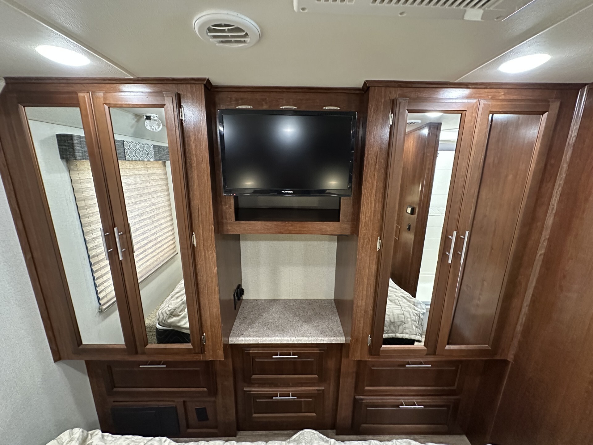 Cozy RV rental bedroom featuring dark wood cabinets, a TV, mirrored wardrobes, and convenient storage drawers.. Forest River Fr3 2019