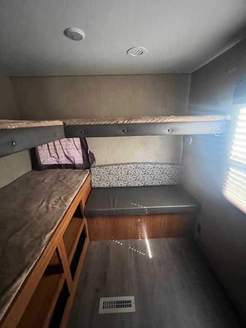 RV rental interior: lower and upper bunk beds, plus an L-shaped dinette seating area with a window. Features wood-look floor.. Starcraft Autumn Ridge 2016
