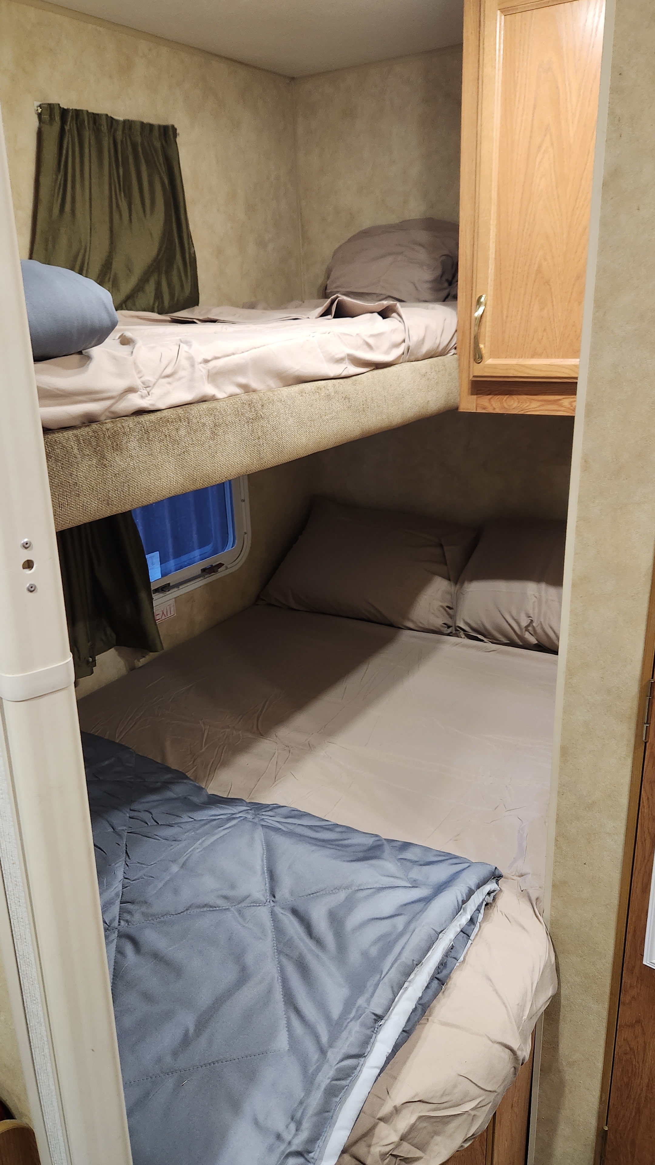 Cozy RV rental bunk beds: a compact sleeping area with pillows, blankets, a window, and a wood cabinet.. Jayco Jay Flight 2006