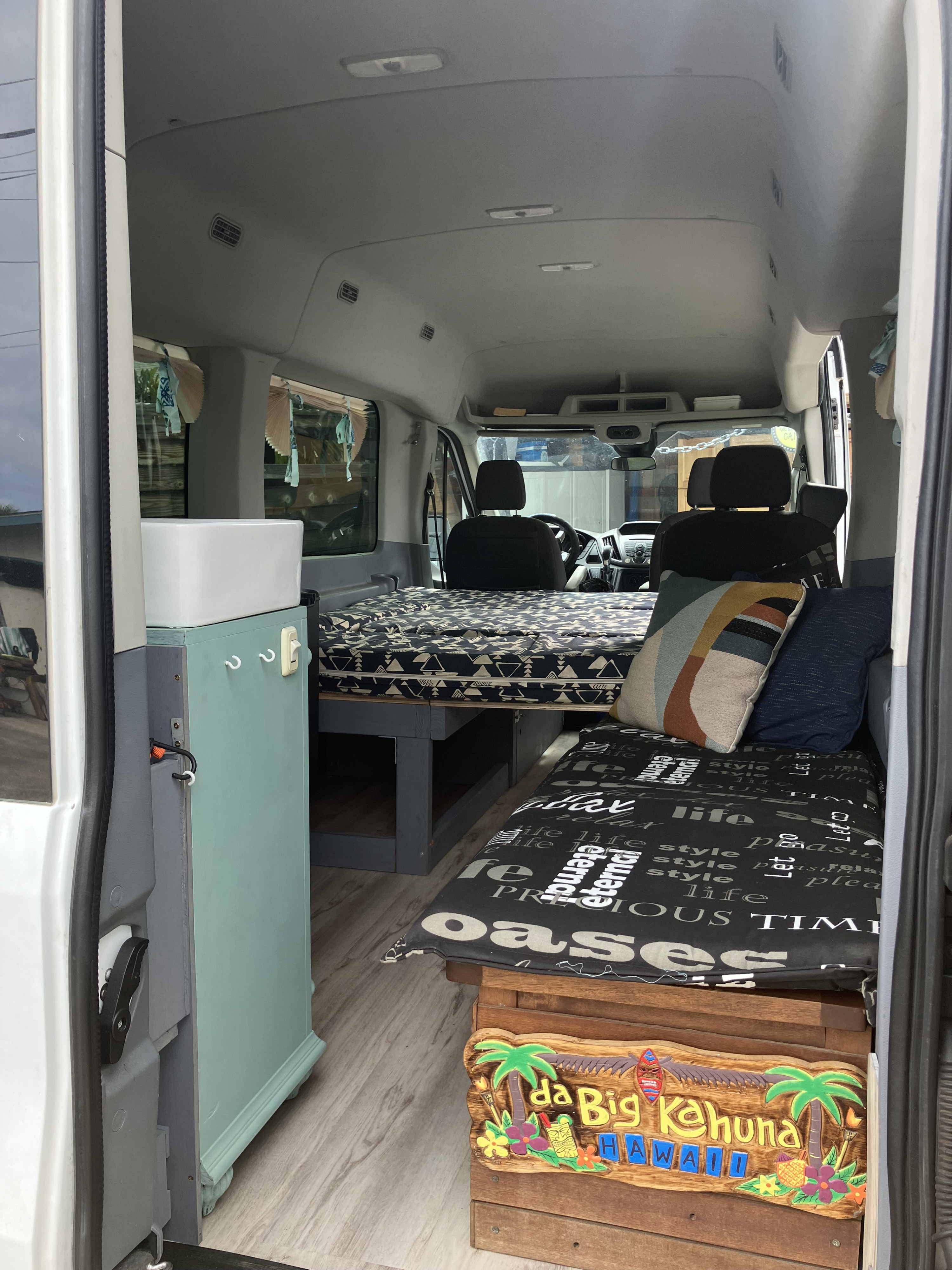 RV rental van conversion interior: a cozy space with a bed, sink, and seating area featuring a Hawaiian theme.. Ford Transit 2018