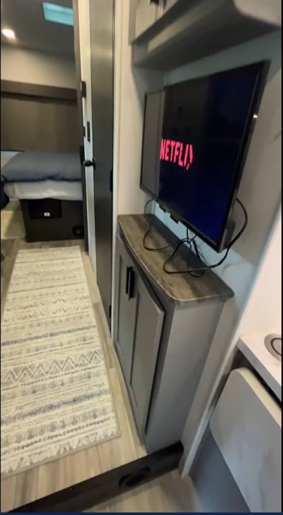 Modern RV rental interior: cozy bedroom, living area with Netflix TV, and patterned floor runner.. Forest River Solera 2023
