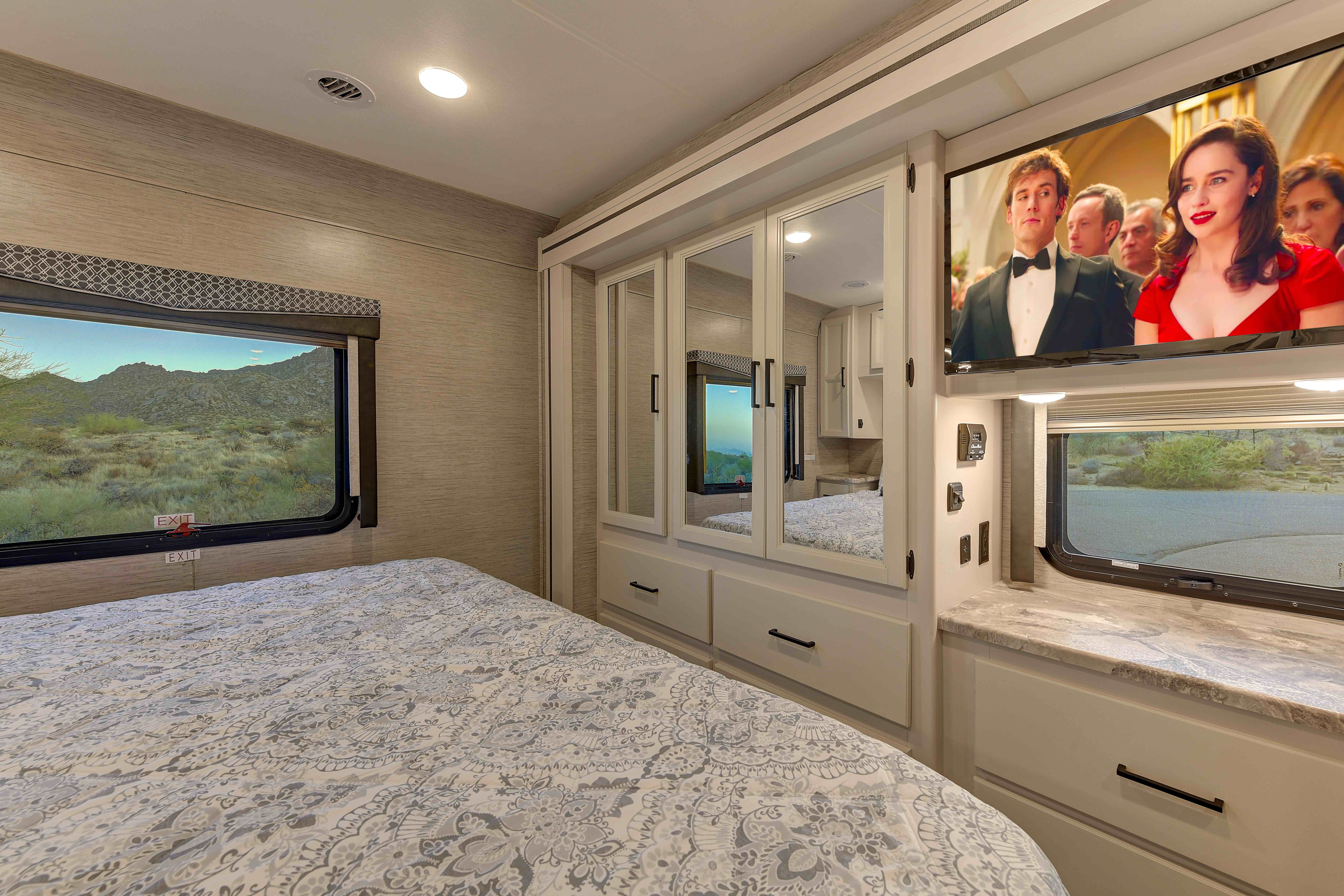 Modern RV rental bedroom with desert views, comfortable bed, TV, and mirrored storage cabinets.. Thor A.C.E. 2022