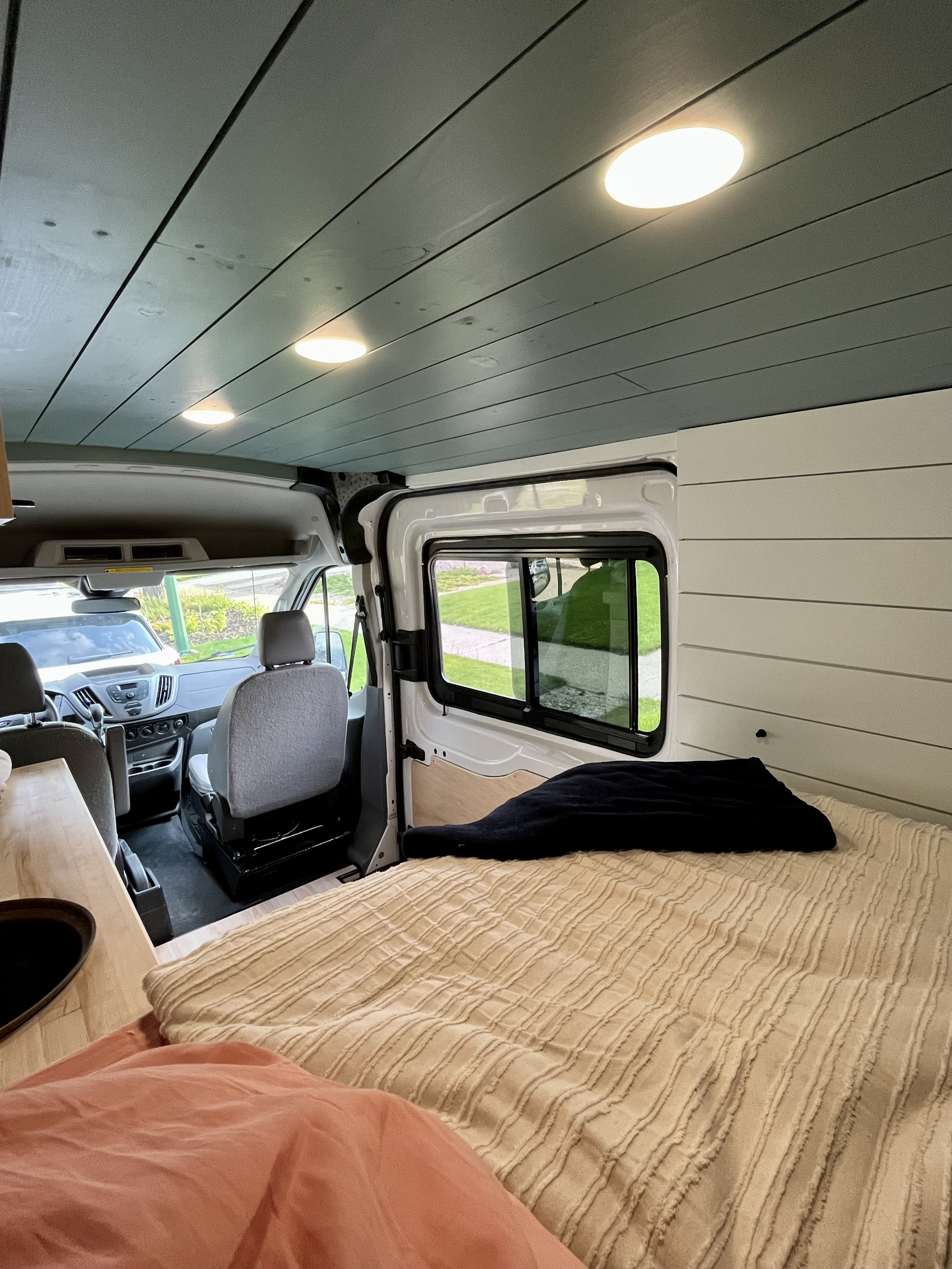 View inside an RV rental camper van, featuring a cozy bed, paneled walls and ceiling, and the front cabin area.. Ford Transit Custom 2018